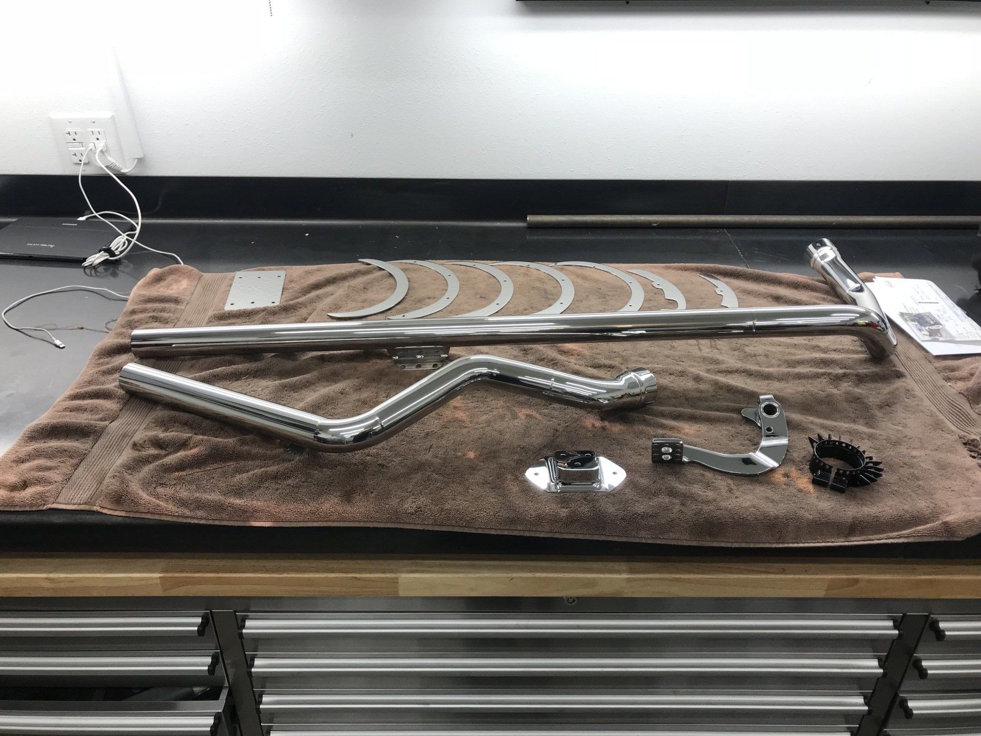 Metal tools and parts laid out on a brown work mat on a workbench, with a framed panel and drawer front below.