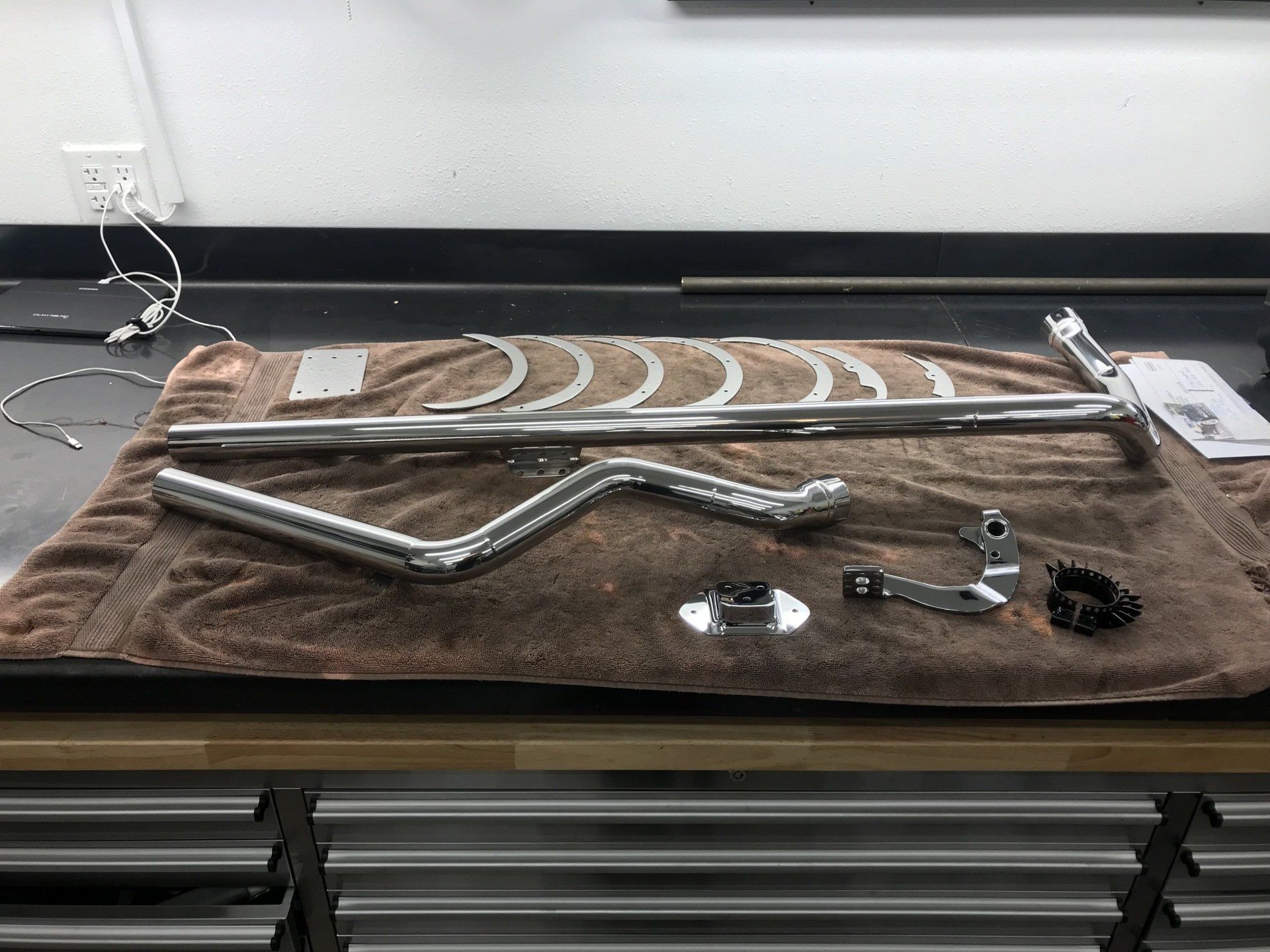 Metal exhaust pipes and small fittings laid out on a brown towel on a workbench.