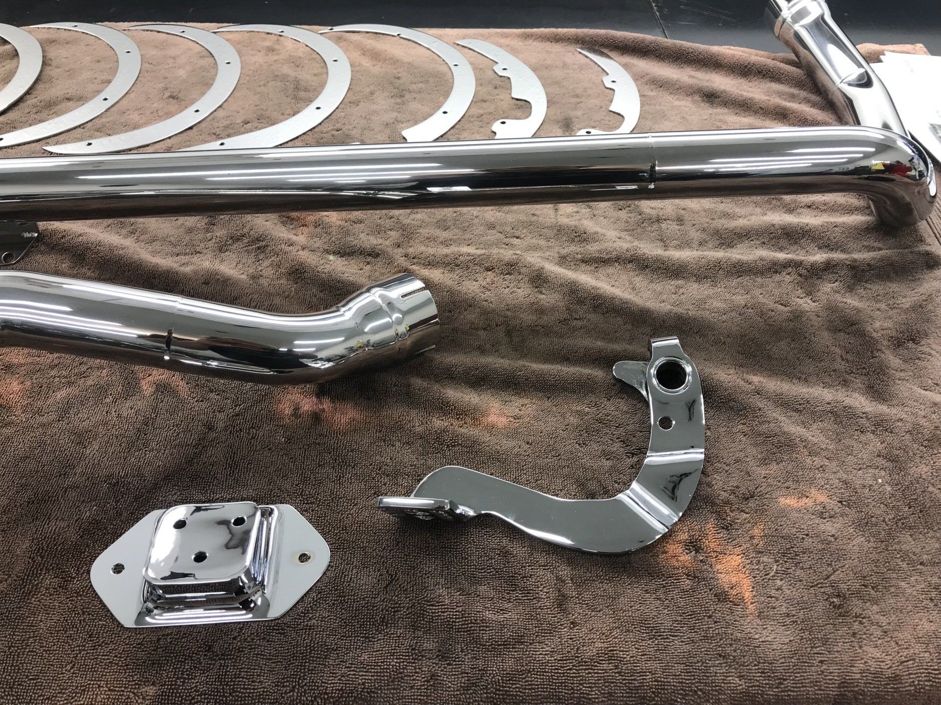 Chrome metal motorcycle parts on a brown towel, including a curved bracket and a small mounting plate.