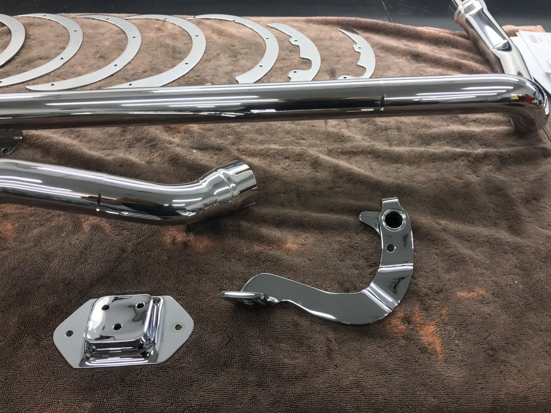 Chrome motorcycle parts laid out on a brown cloth, including exhaust pipes and metal brackets.