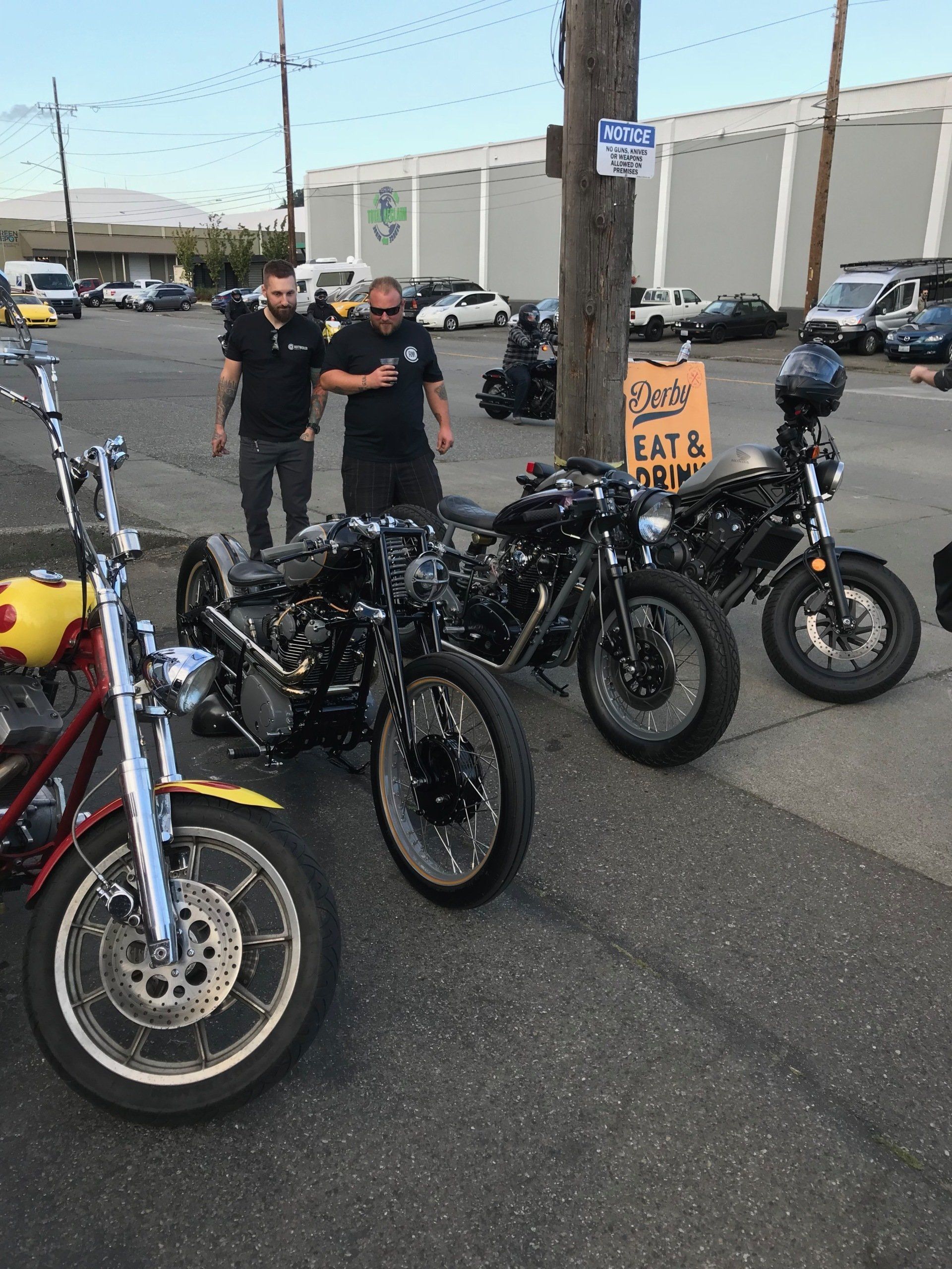 Motorcycles lined up at an outdoor gathering with two people standing behind them