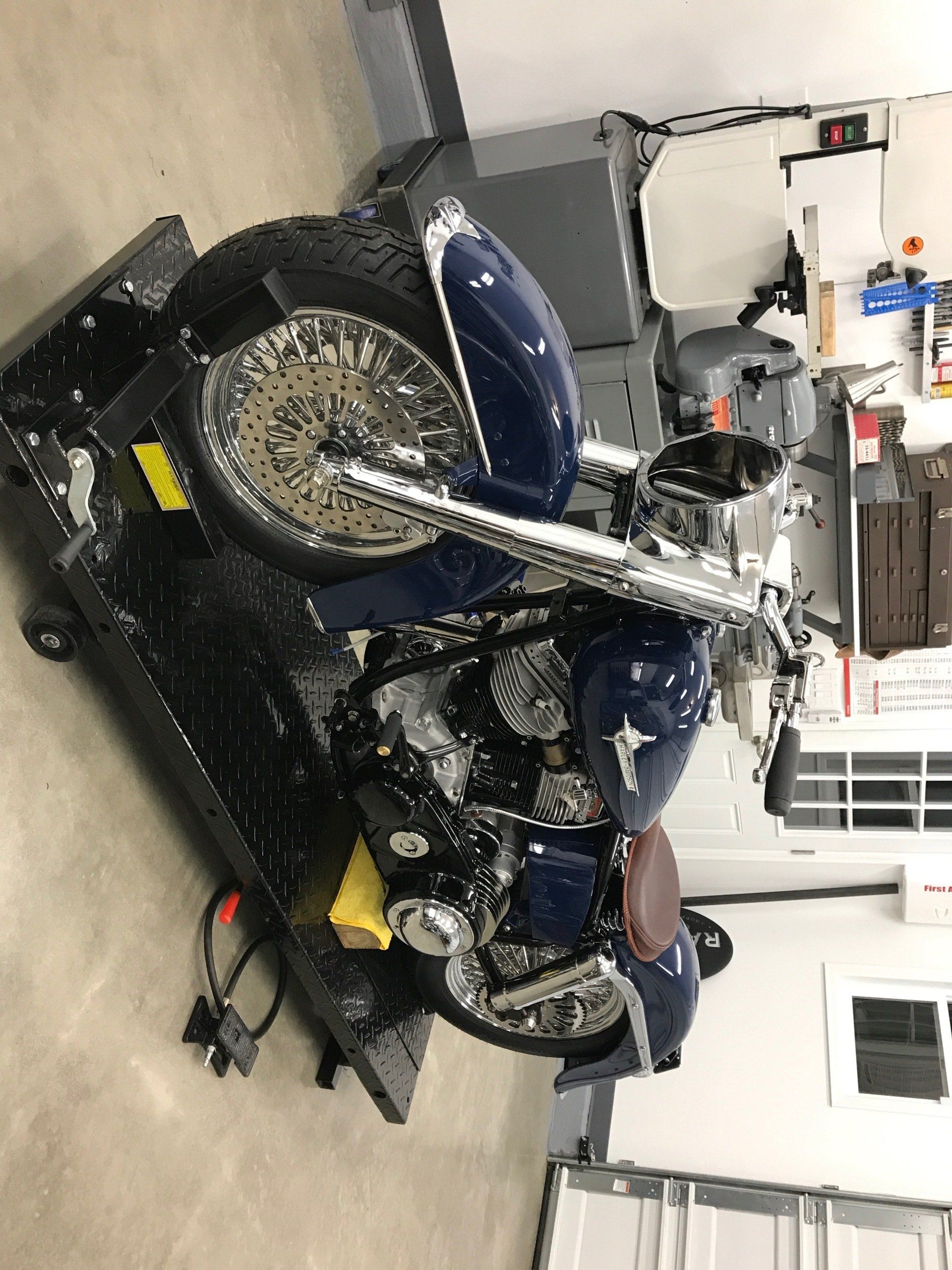 Blue motorcycle on a maintenance stand in a garage, with tools and equipment nearby.