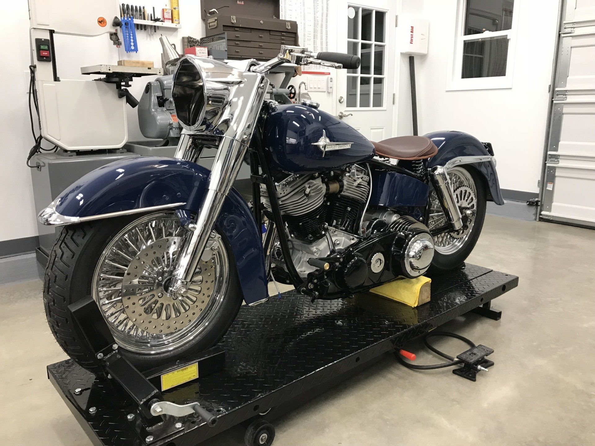 Blue motorcycle on a lift in a garage workshop, with chrome details and a sidecar-like seat.