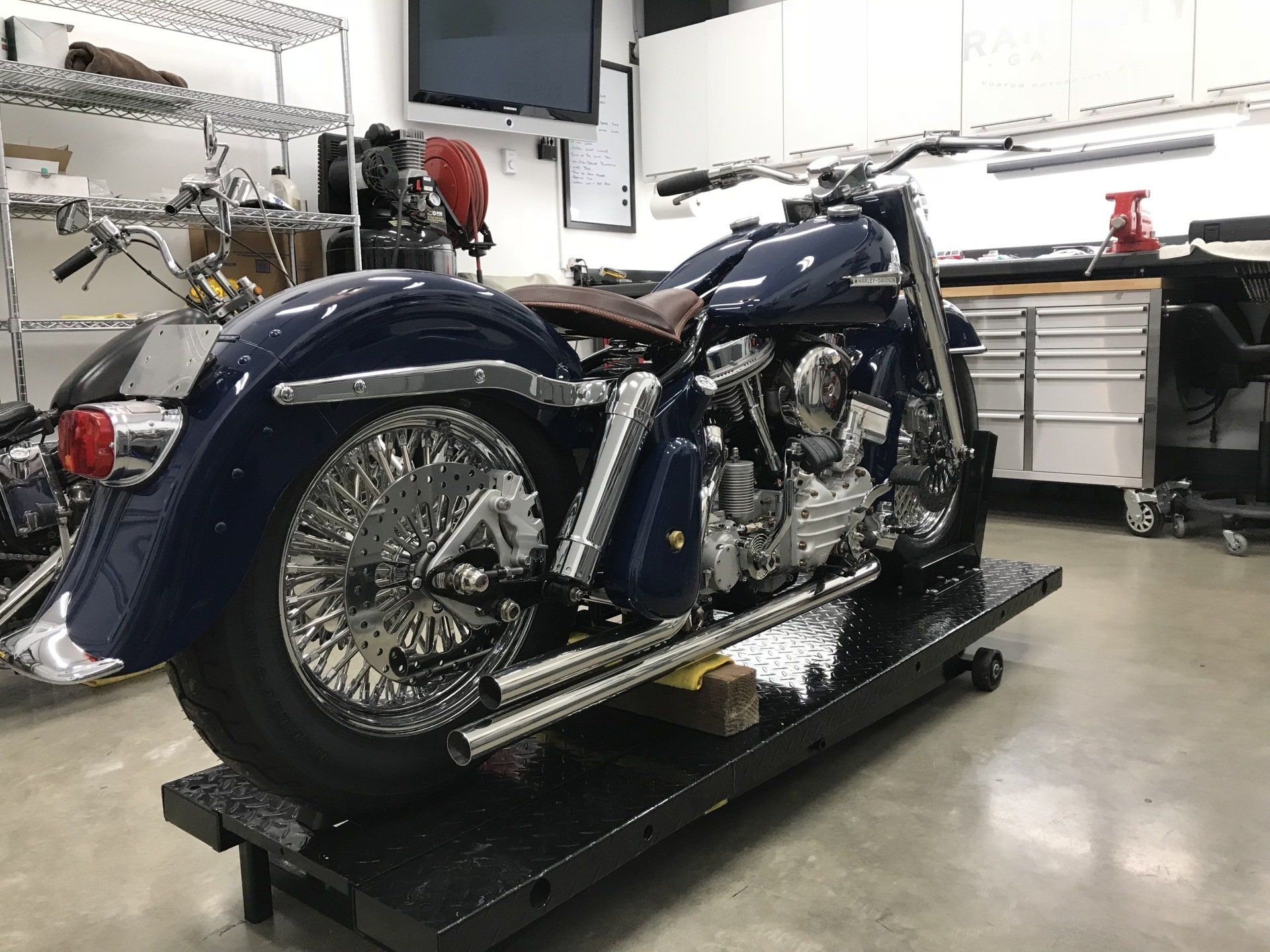 Blue custom motorcycle on a lift in a workshop garage with tools and cabinets in the background