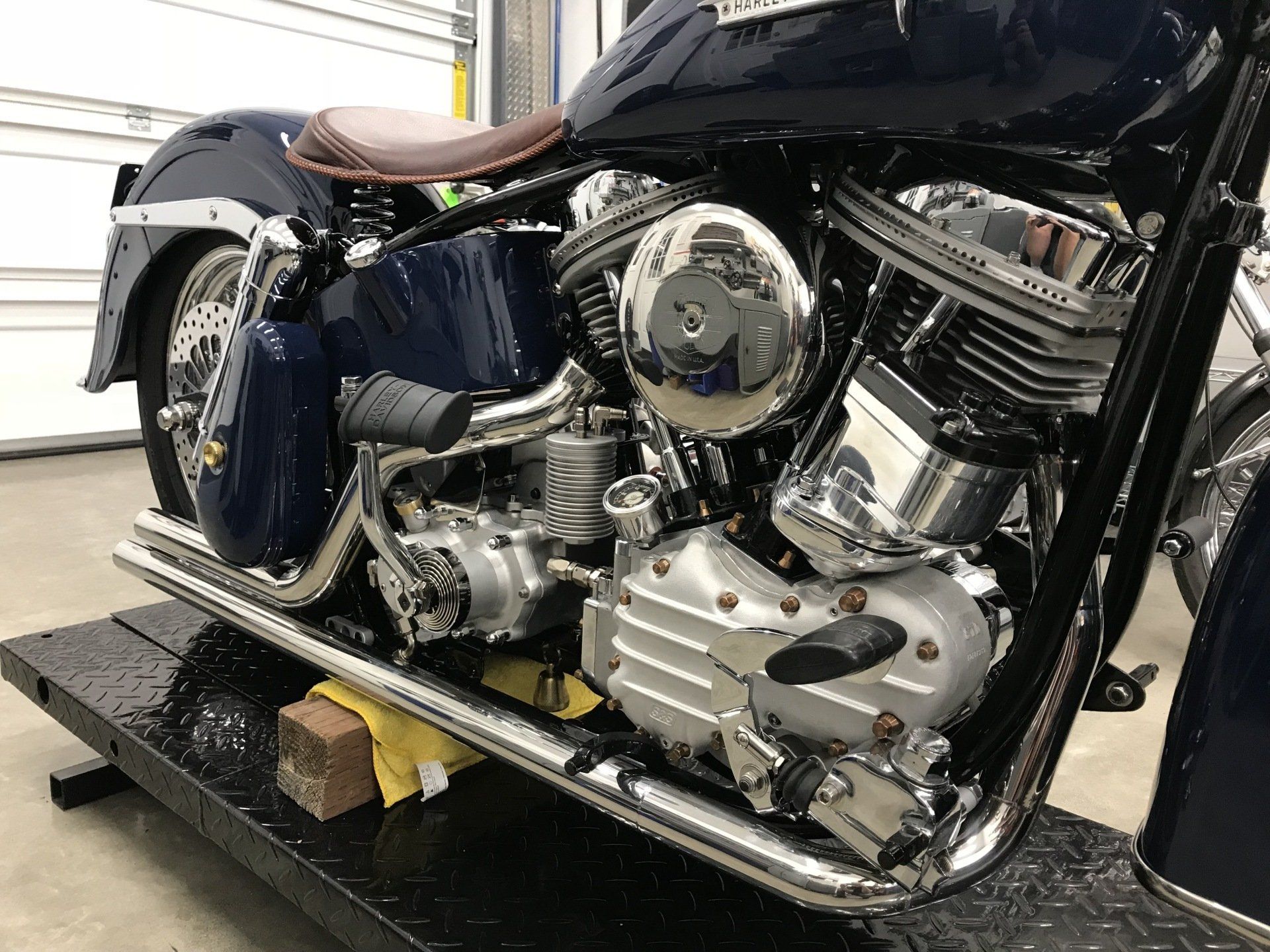 Close-up of a black motorcycle engine and chrome exhaust with a brown seat in a garage