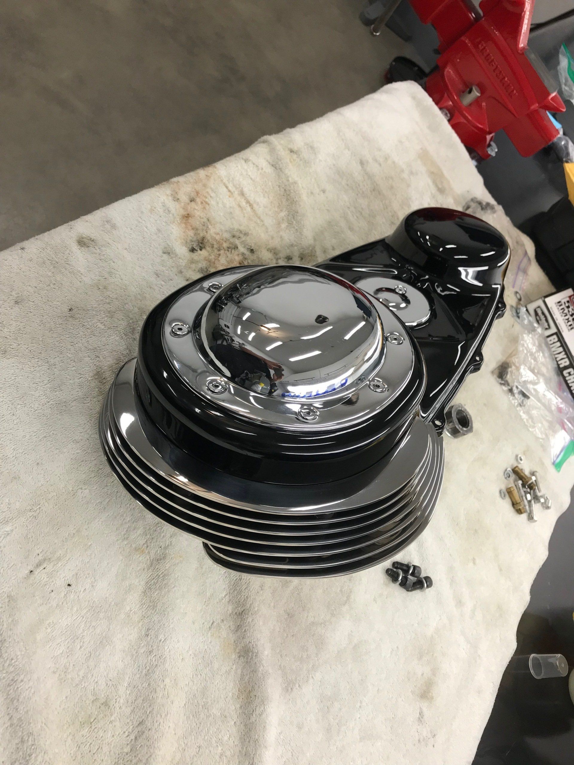 Black and chrome motorcycle engine cover on a shop towel, with bolts nearby.