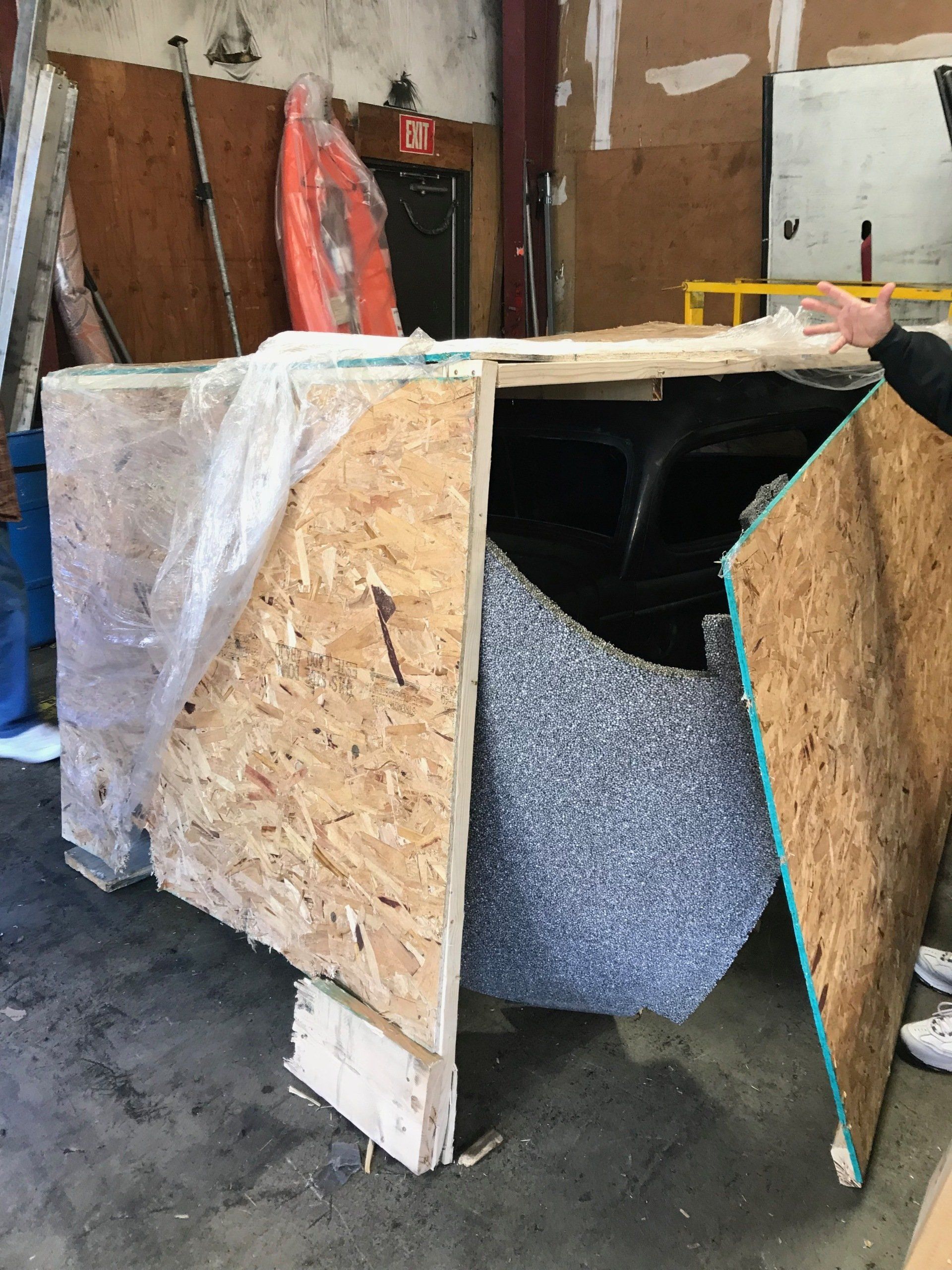 Wooden crate with insulation foam inside in a workshop, open front panel leaning outward.