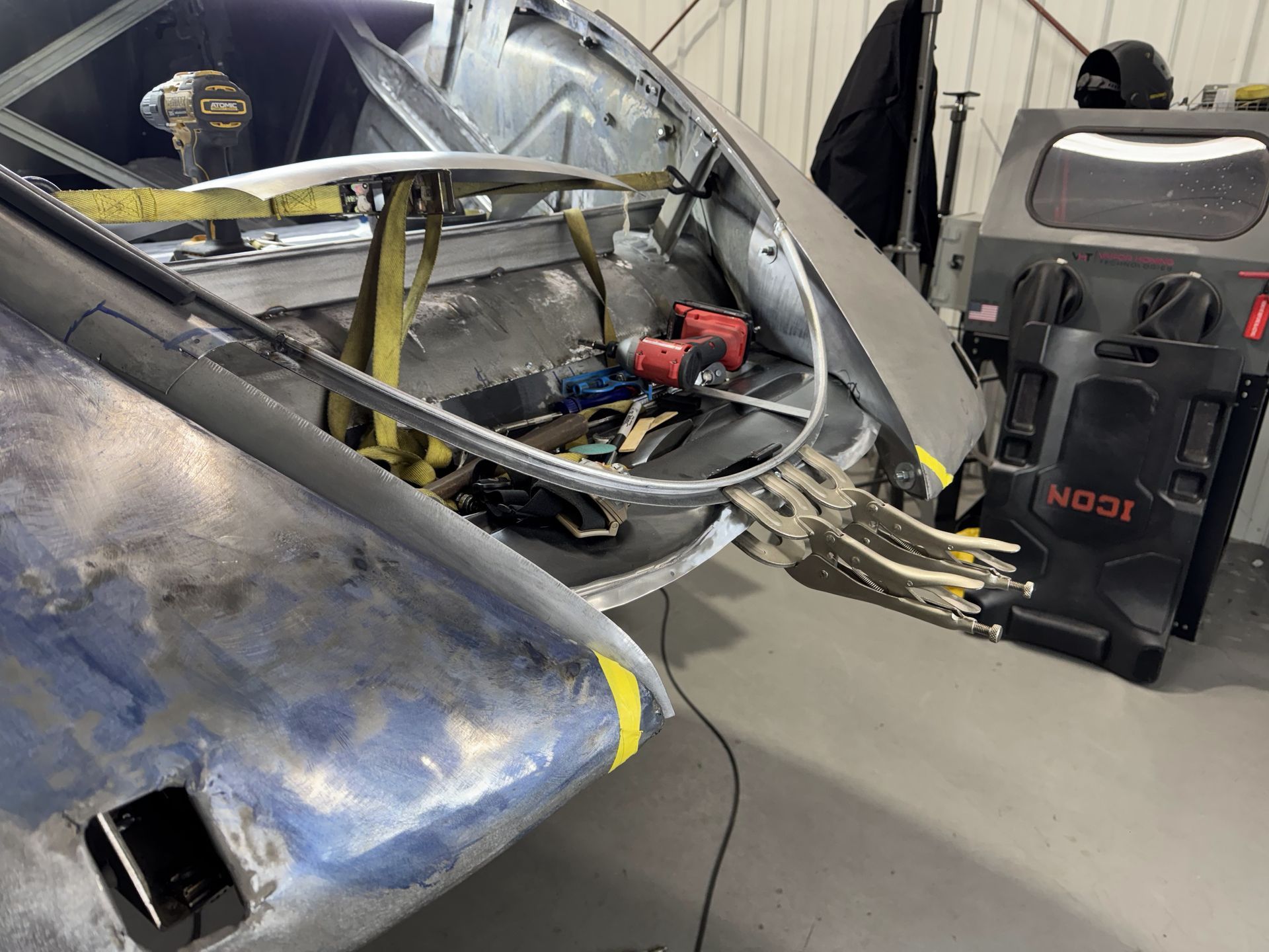 Damaged blue car in a garage with exposed engine and a red diagnostic machine nearby