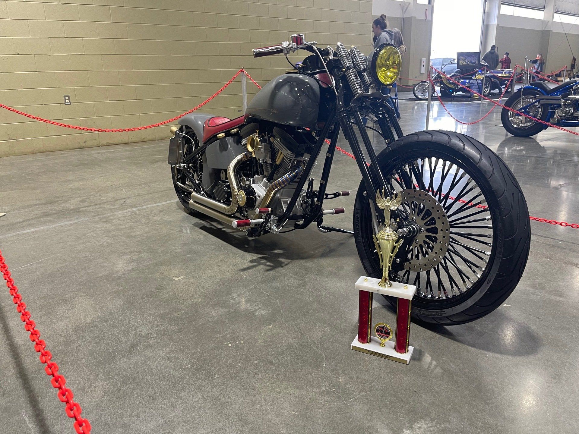 Black custom motorcycle with large front wheel on display in an indoor showroom.