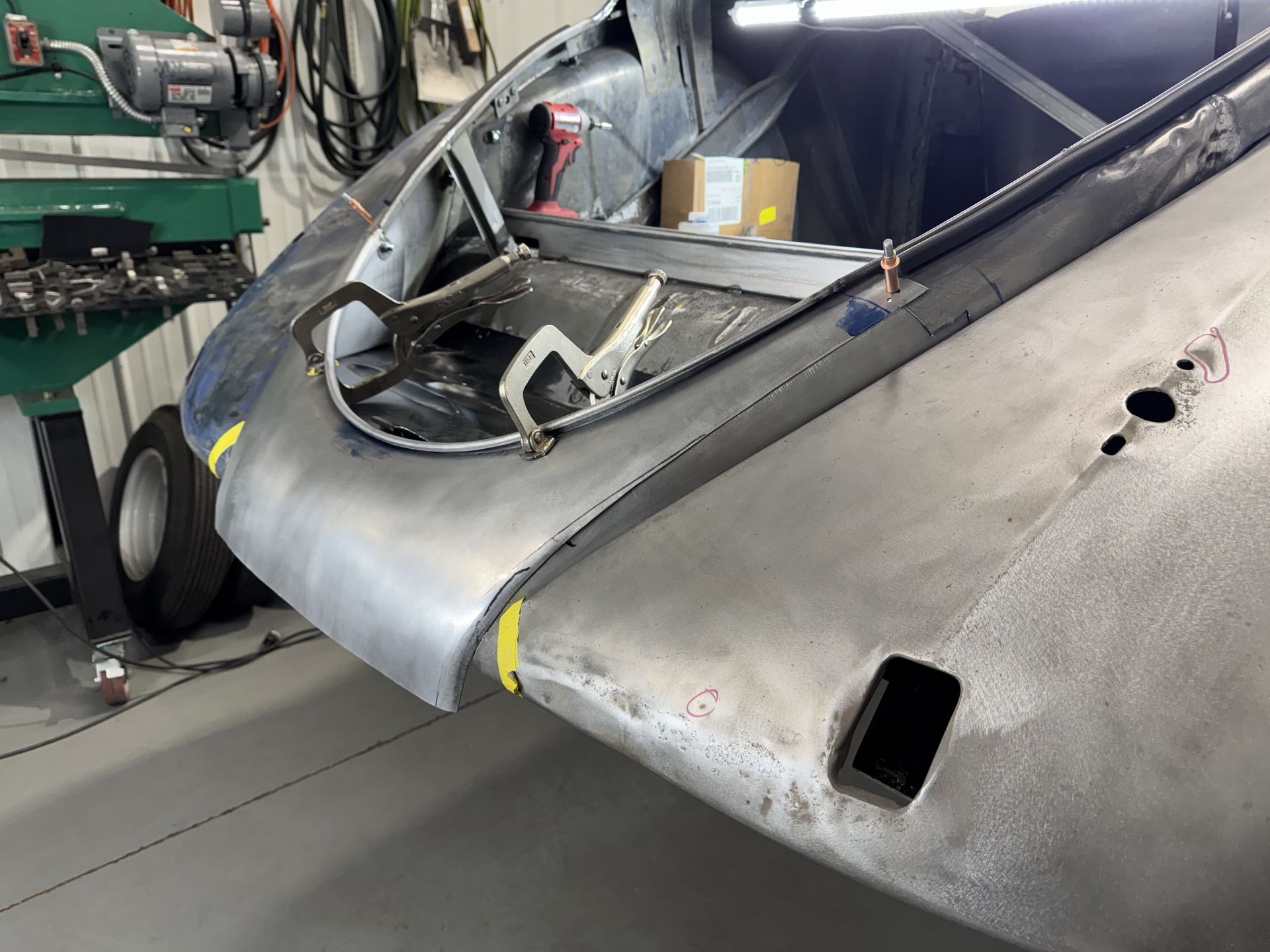 Damaged silver aircraft fuselage in a workshop, with open cockpit and visible dents and holes
