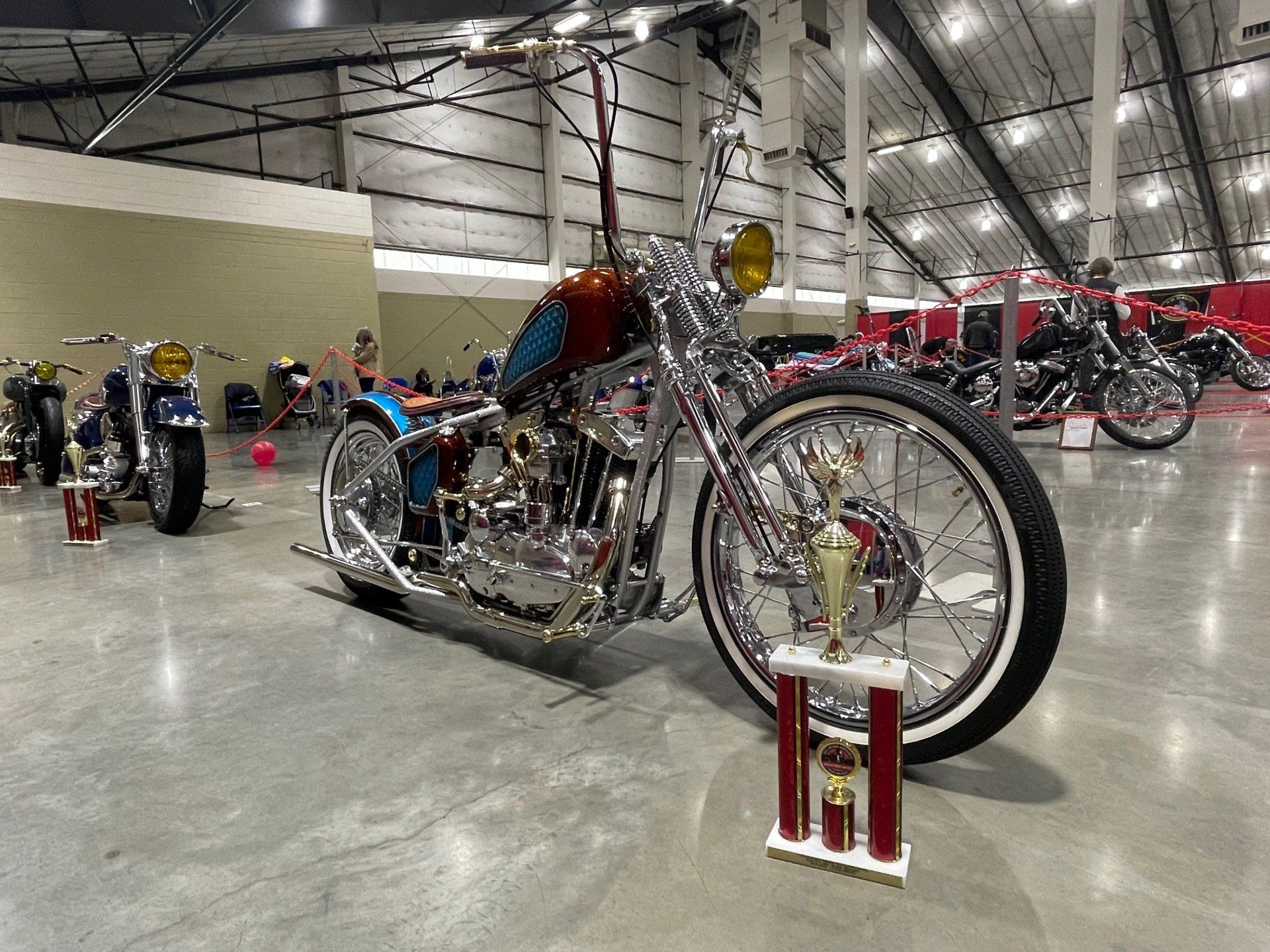 Custom chopper motorcycle on display in a warehouse with other bikes in the background