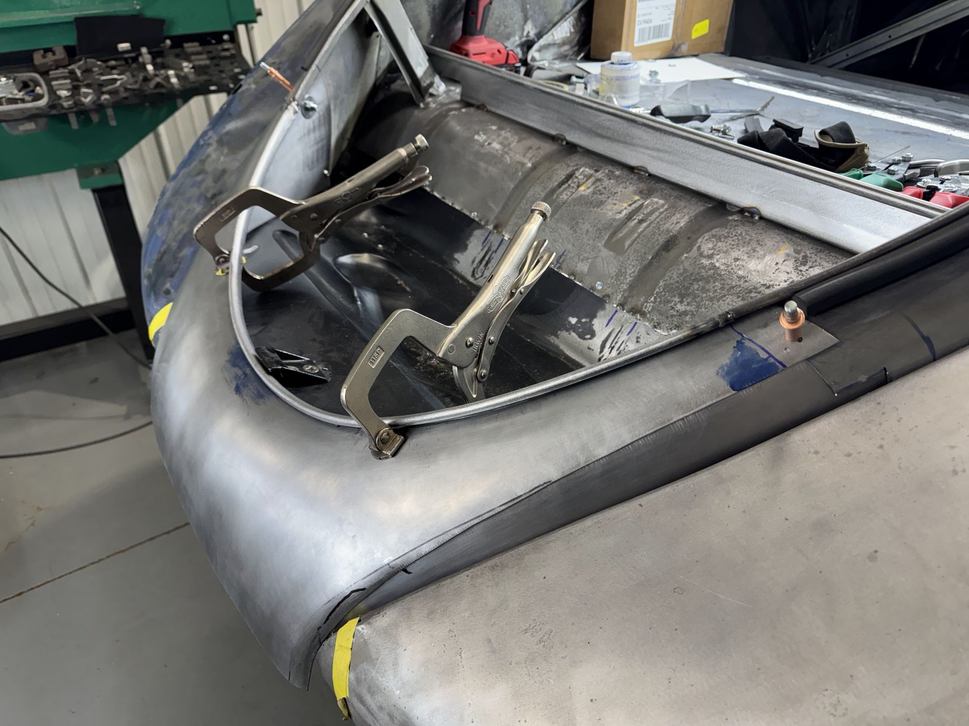 Damaged car hood in a workshop, with exposed frame and detached black panel.