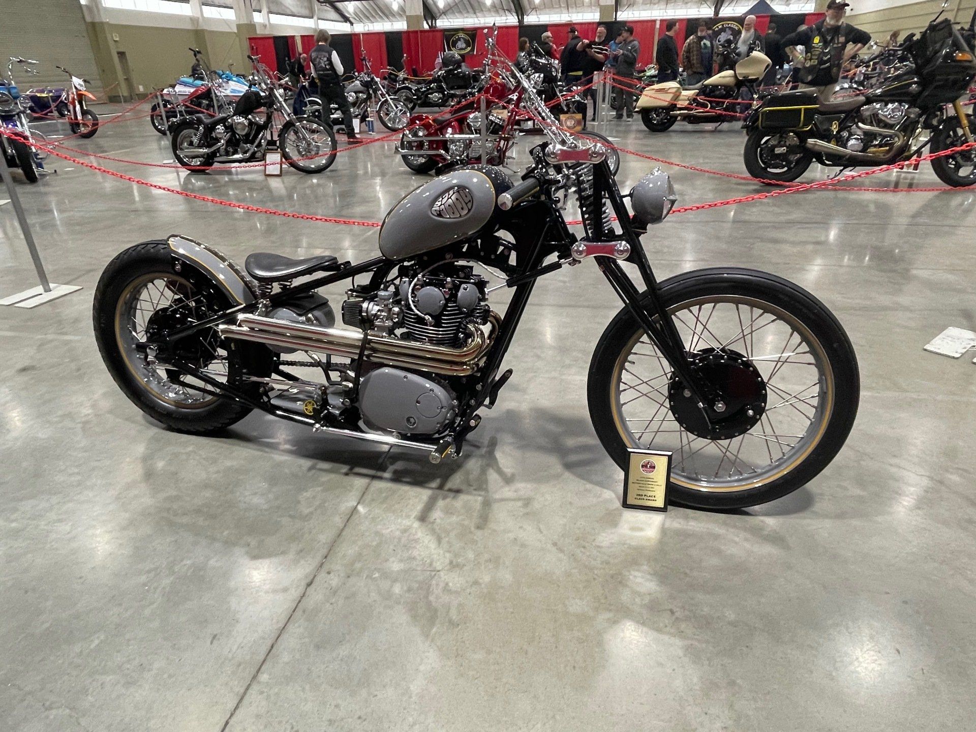Custom black vintage motorcycle on display at an indoor showroom, with other bikes in the background