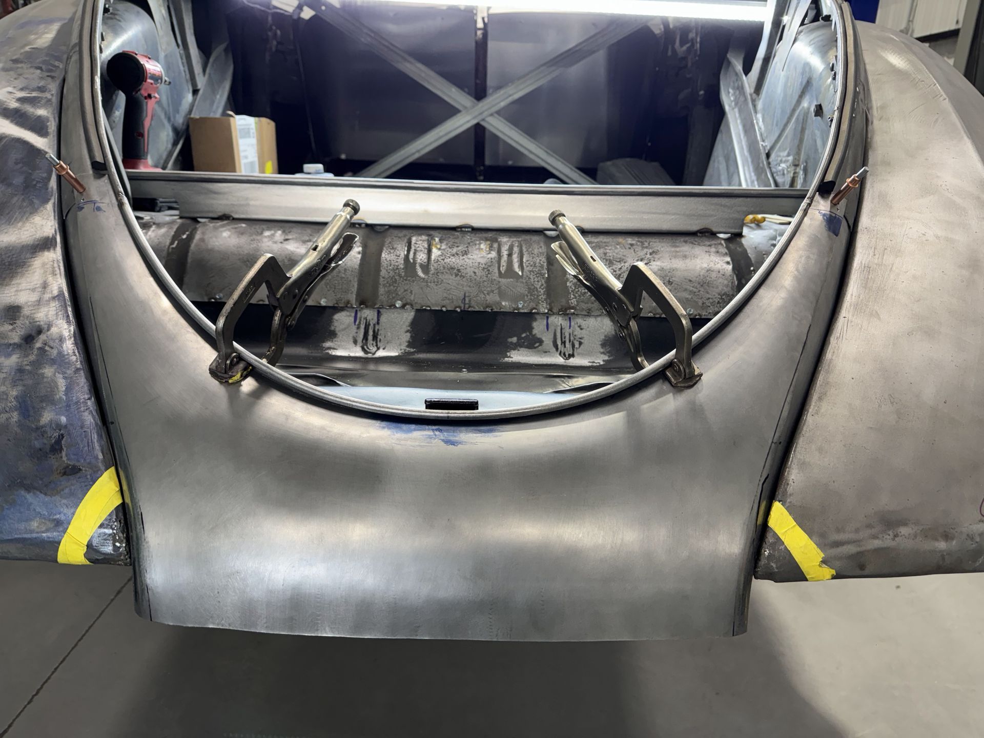 Front view of a gray metal car body shell in a workshop, with exposed interior and frame.