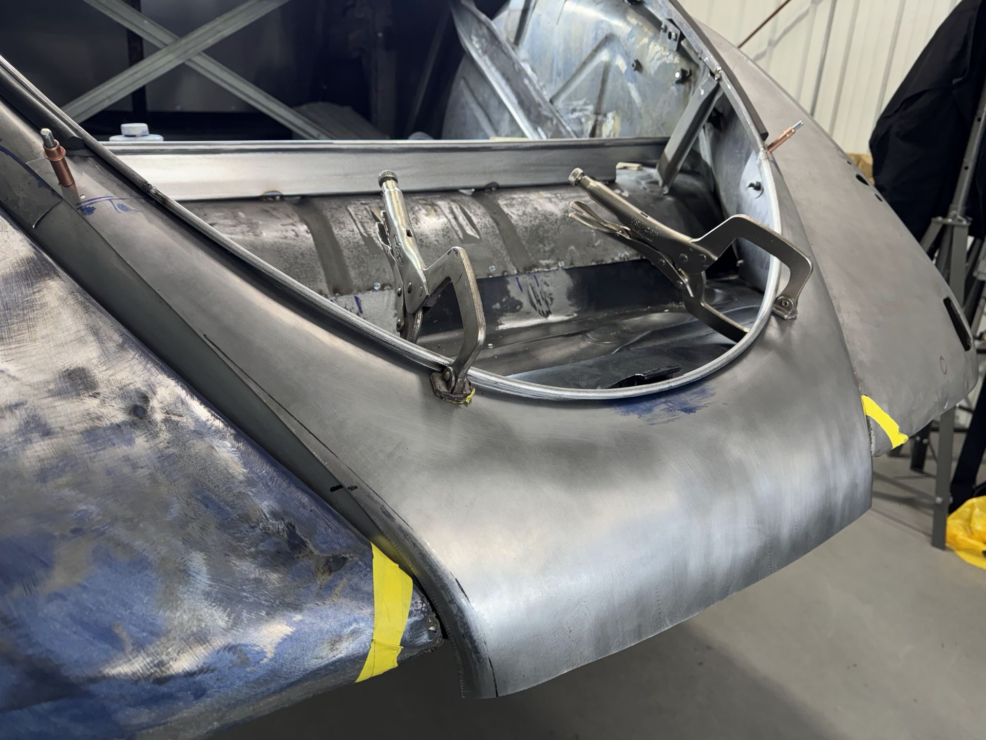 Damaged gray vehicle front end with a missing hood and exposed frame in a workshop