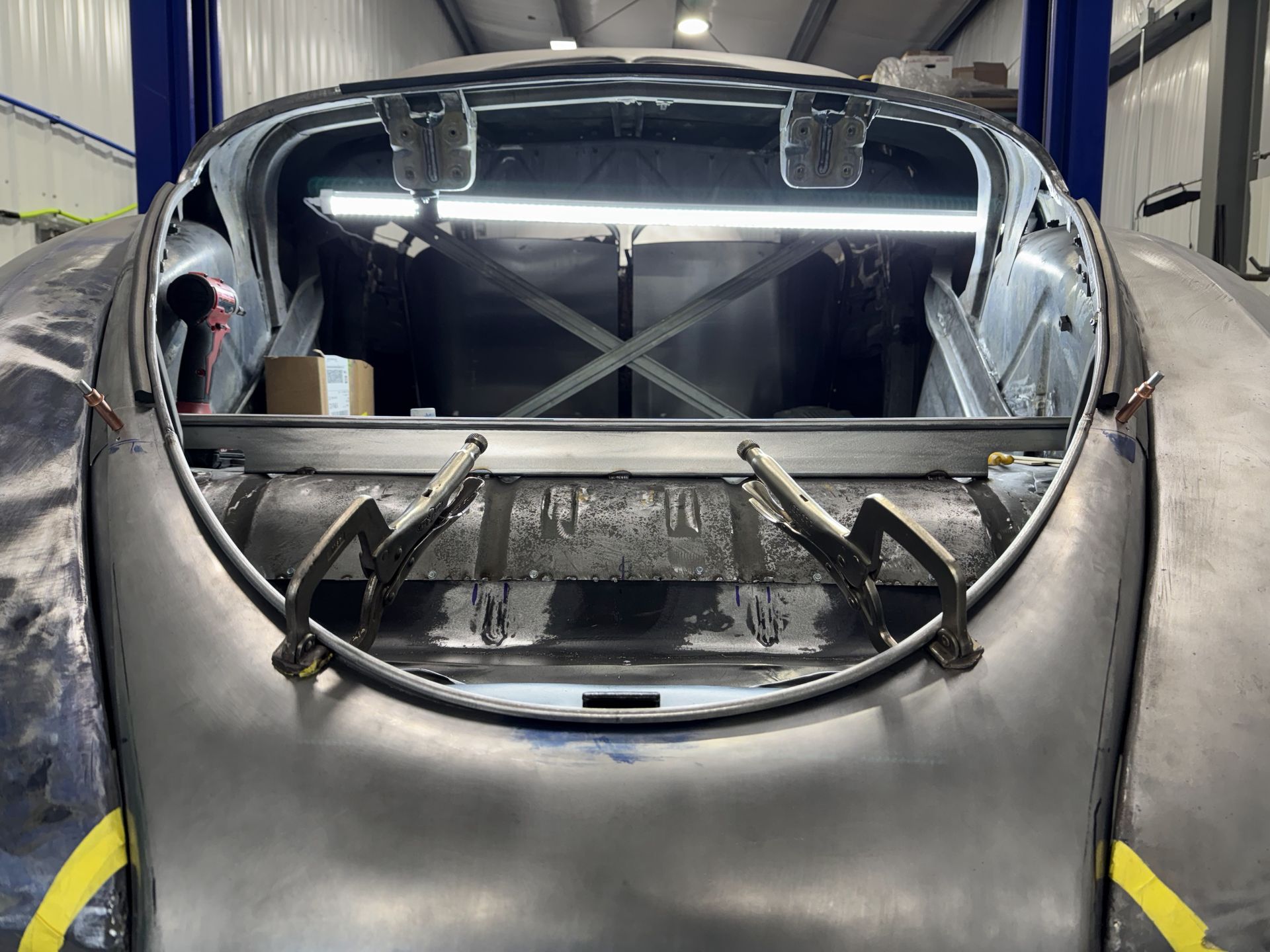 Silver race car body shell in a workshop, viewed from the front with interior roll cage visible