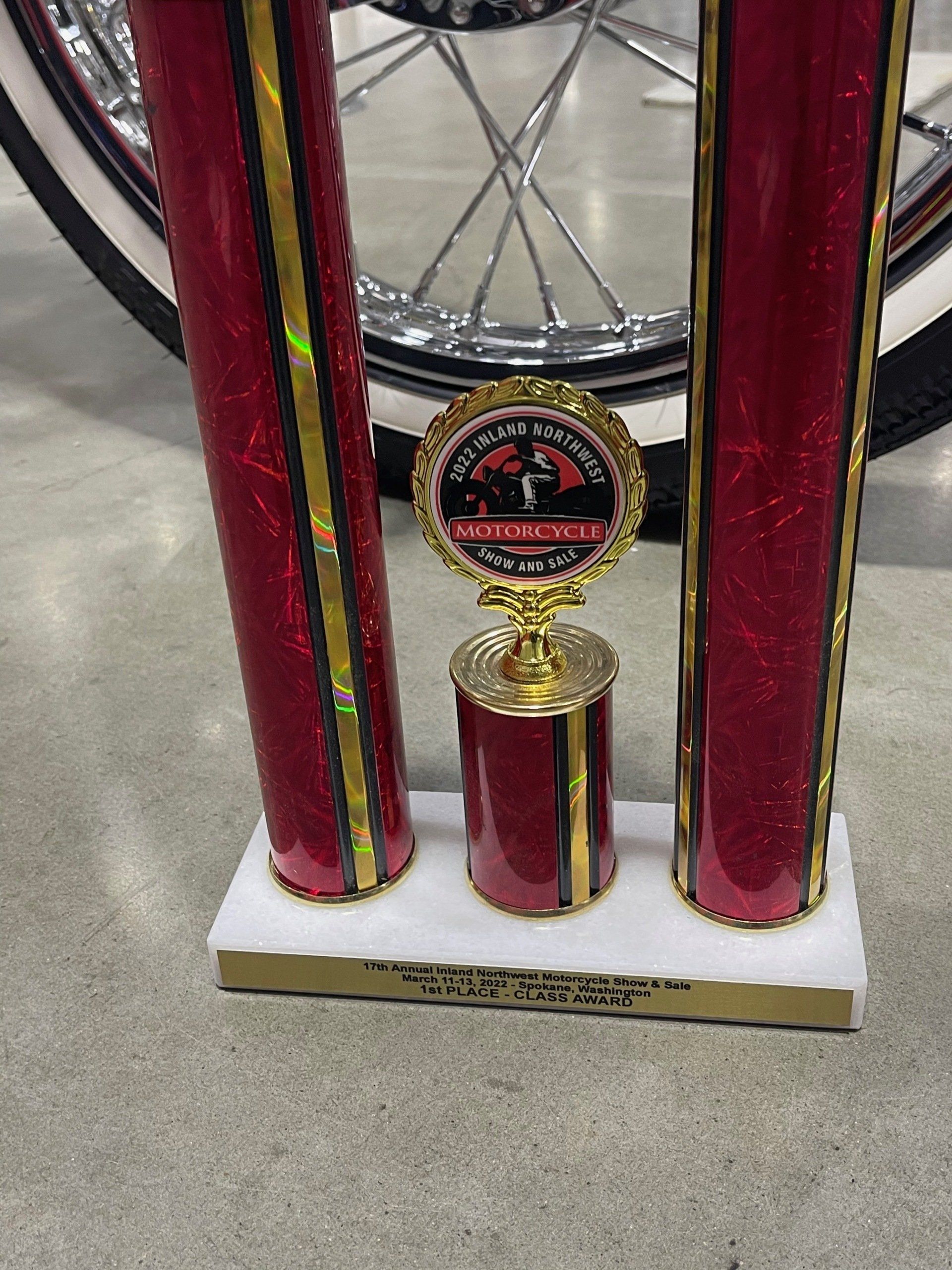 Trophy with red-and-gold columns and a medal centerpiece on a white base, standing on a floor.