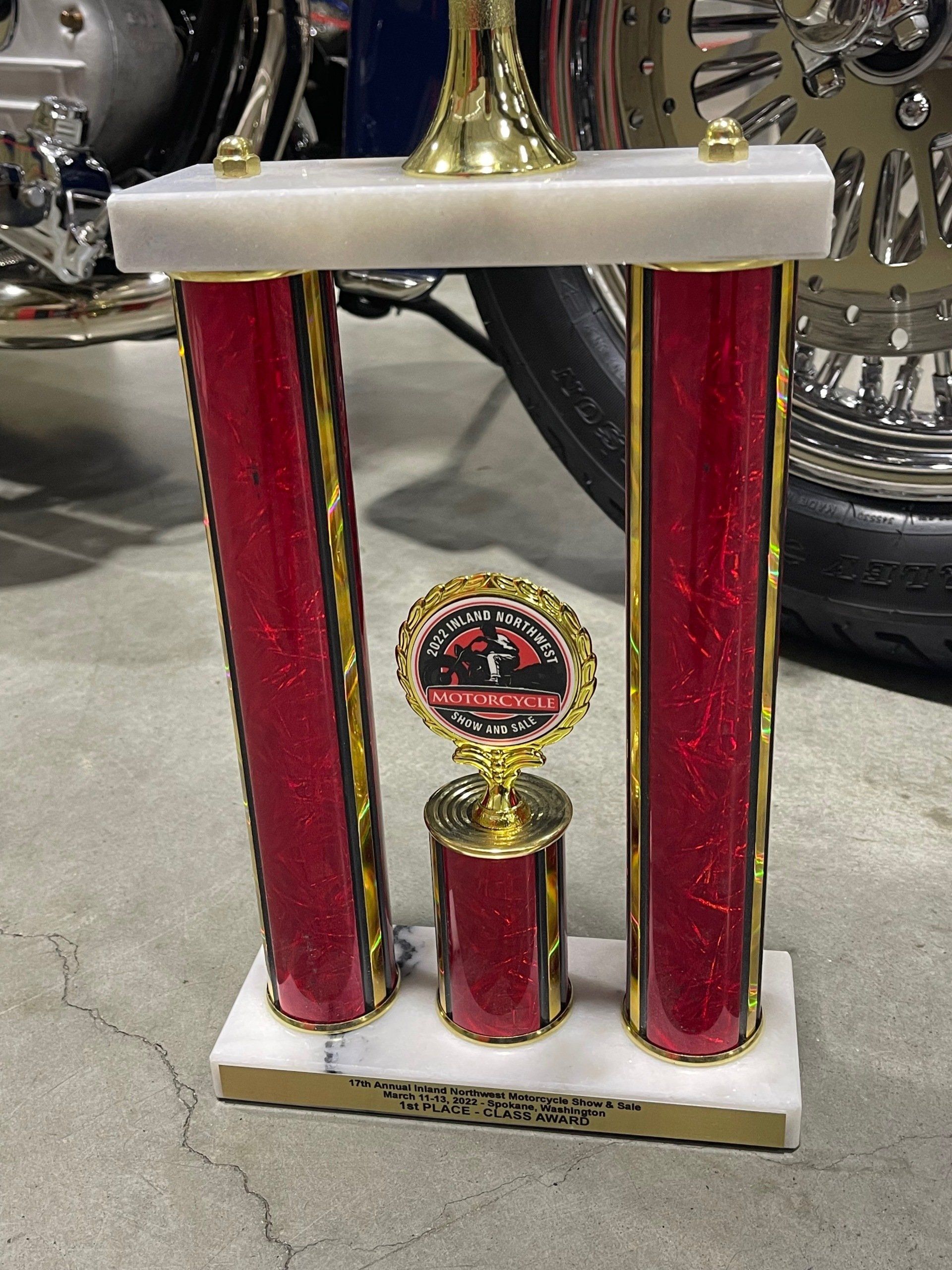 Red and gold trophy with a circular emblem, standing on a white base in a display setting