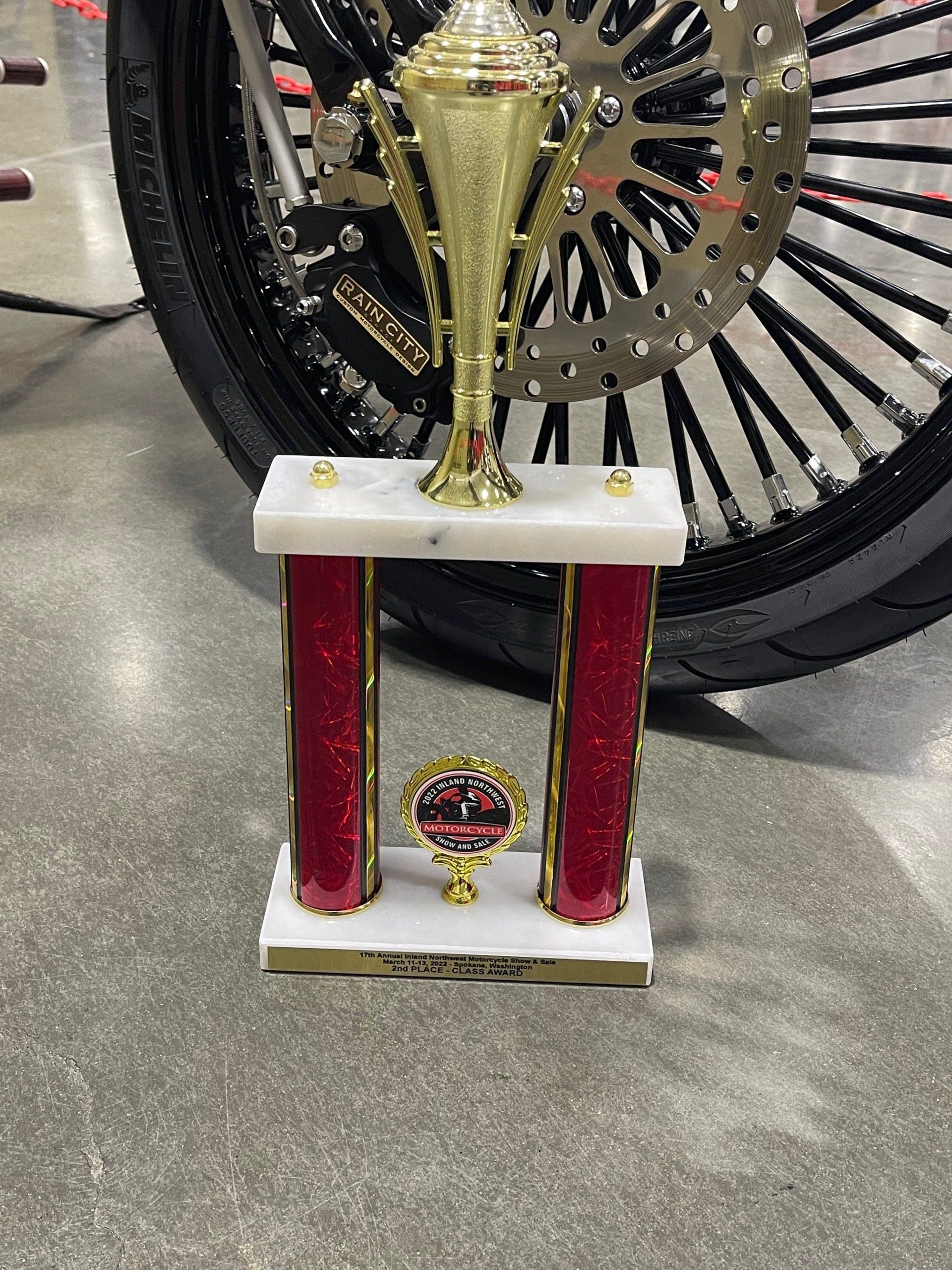 Gold trophy with red columns in front of a car wheel on a concrete floor
