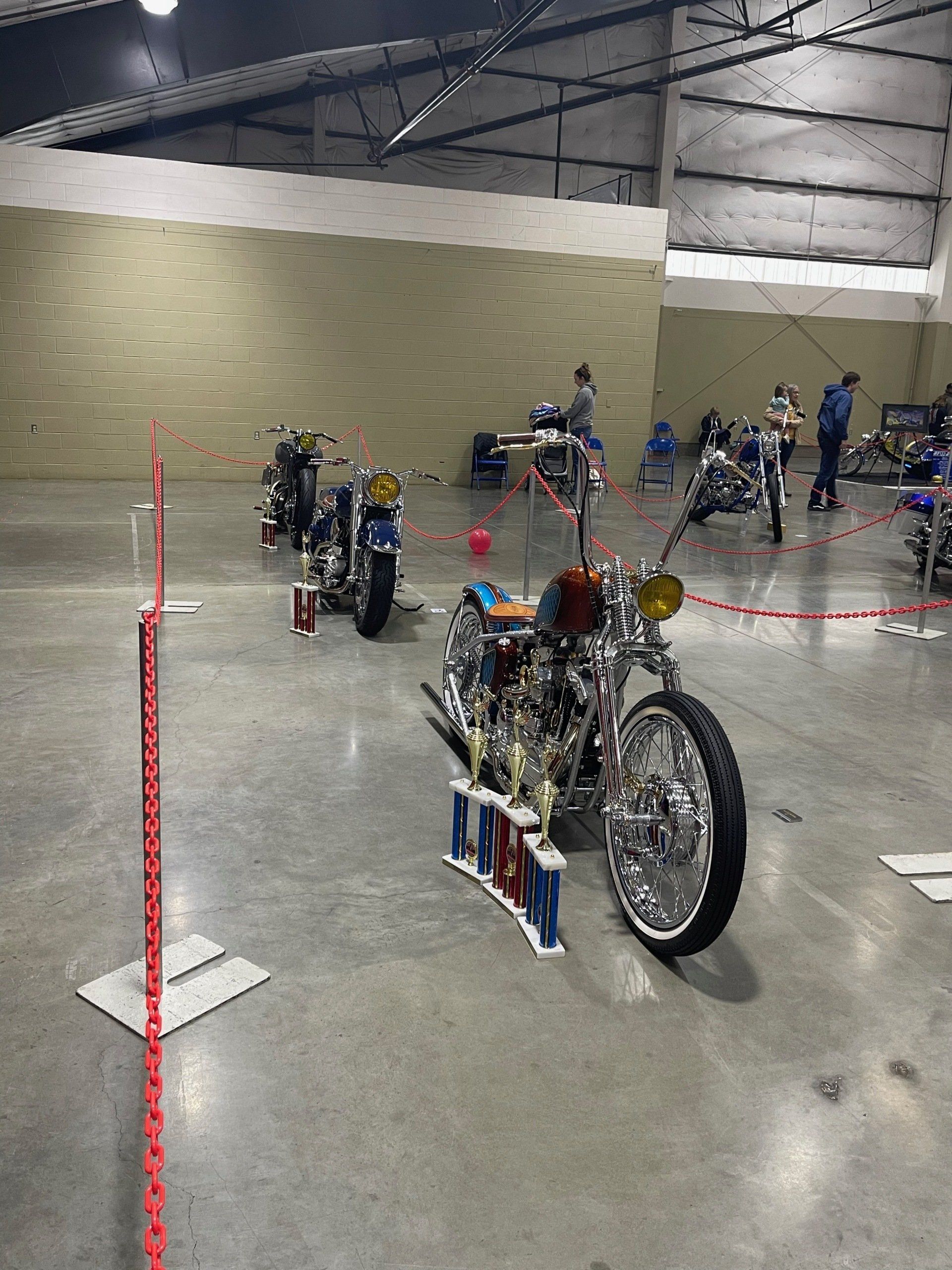 Motorcycles displayed in a large indoor exhibition hall with red stanchions and polished concrete floor