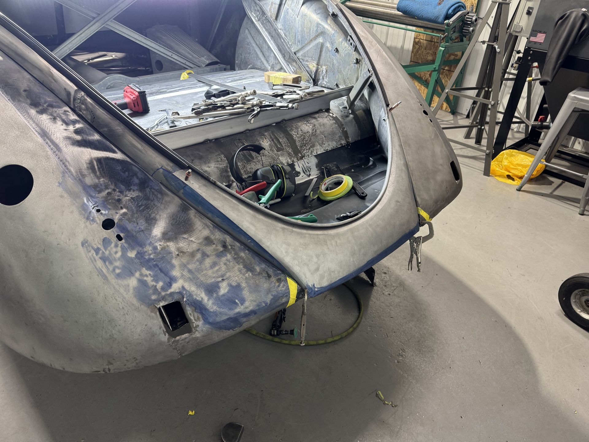 Damaged car bumper and rear panel in a workshop, with tools inside the open trunk area