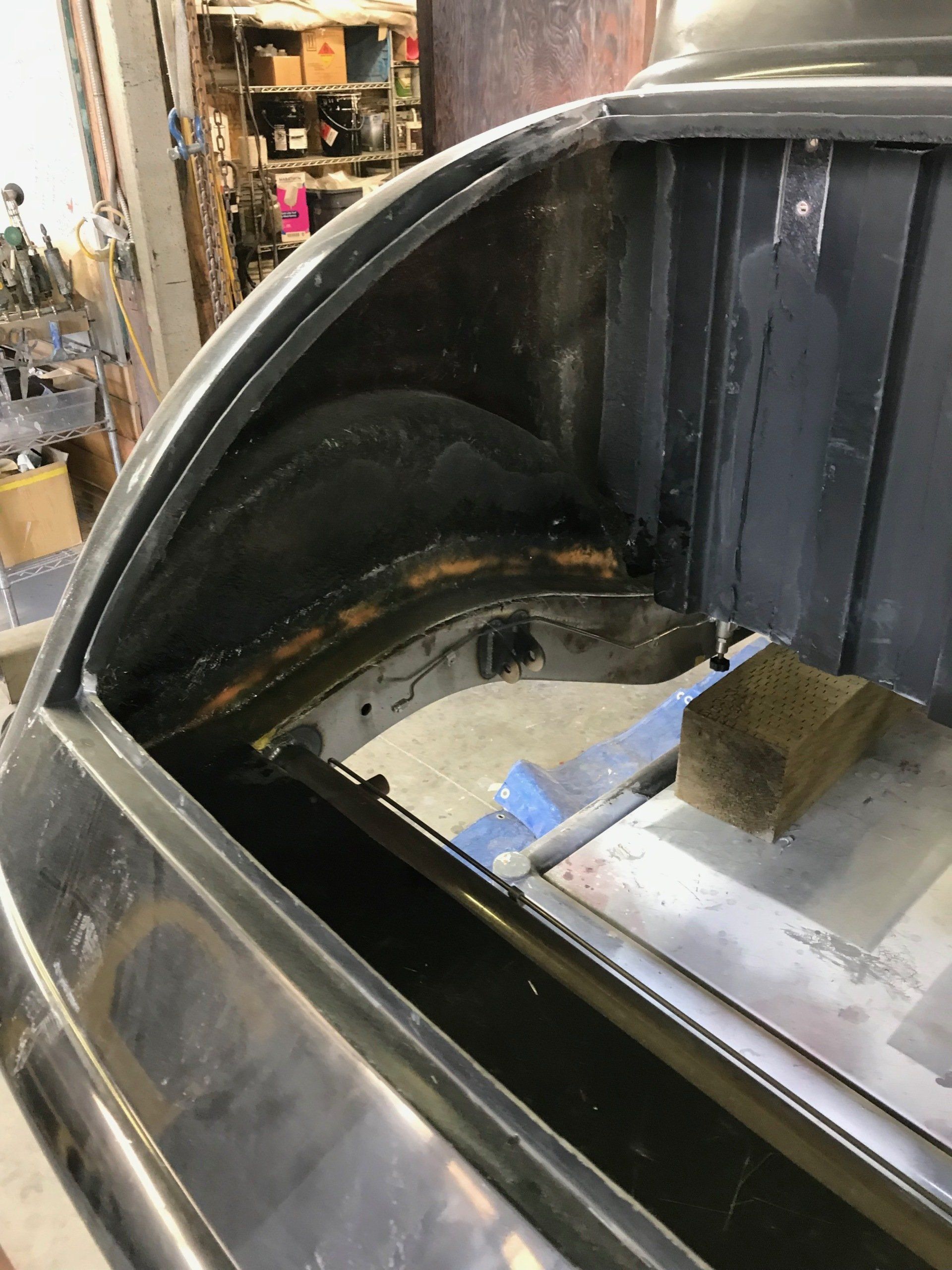 Close-up of a black metal tank interior with a curved opening and a small taped block inside, in a workshop.