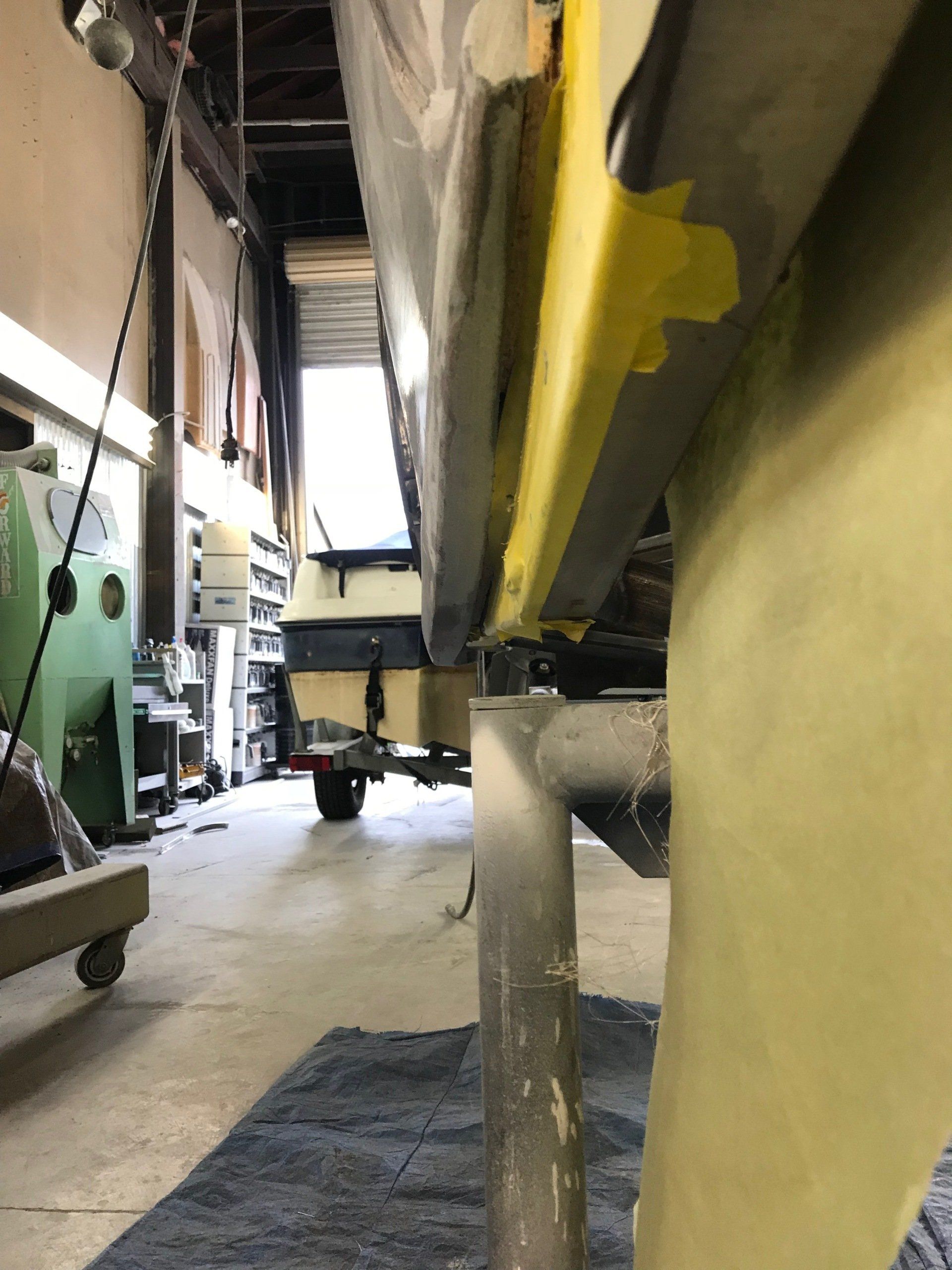 Narrow industrial aisle with large yellow and green machinery and a wheeled cart in the background