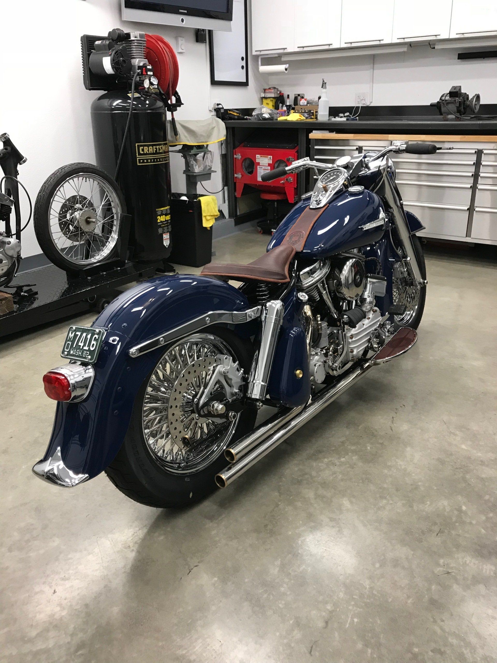 Blue custom motorcycle parked in a garage, with chrome details and a brown leather seat.