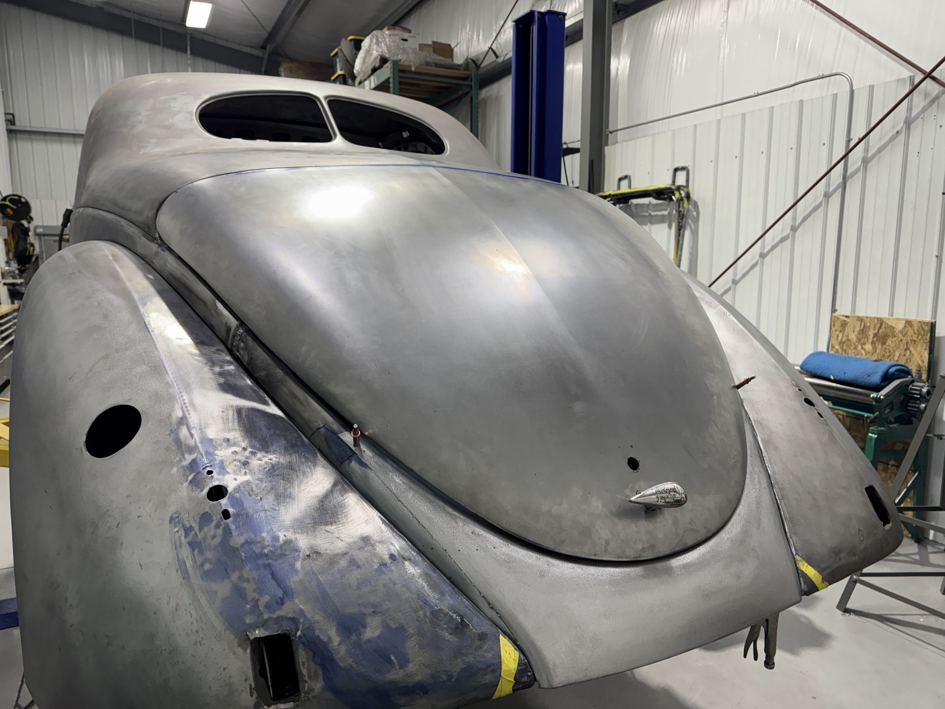 Gray vintage car body shell in a workshop, viewed from the front-left side.