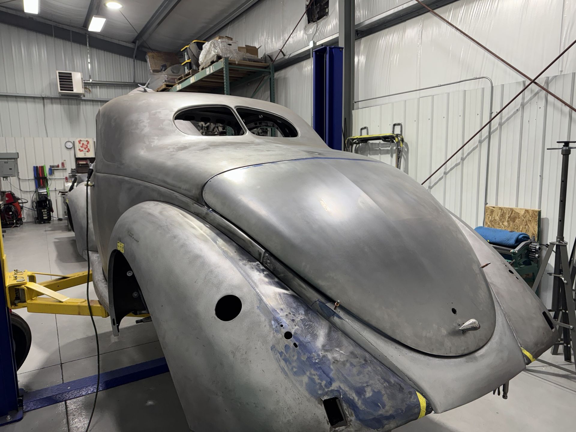 Gray classic car body shell under restoration in a workshop, with primer and exposed metal panels.