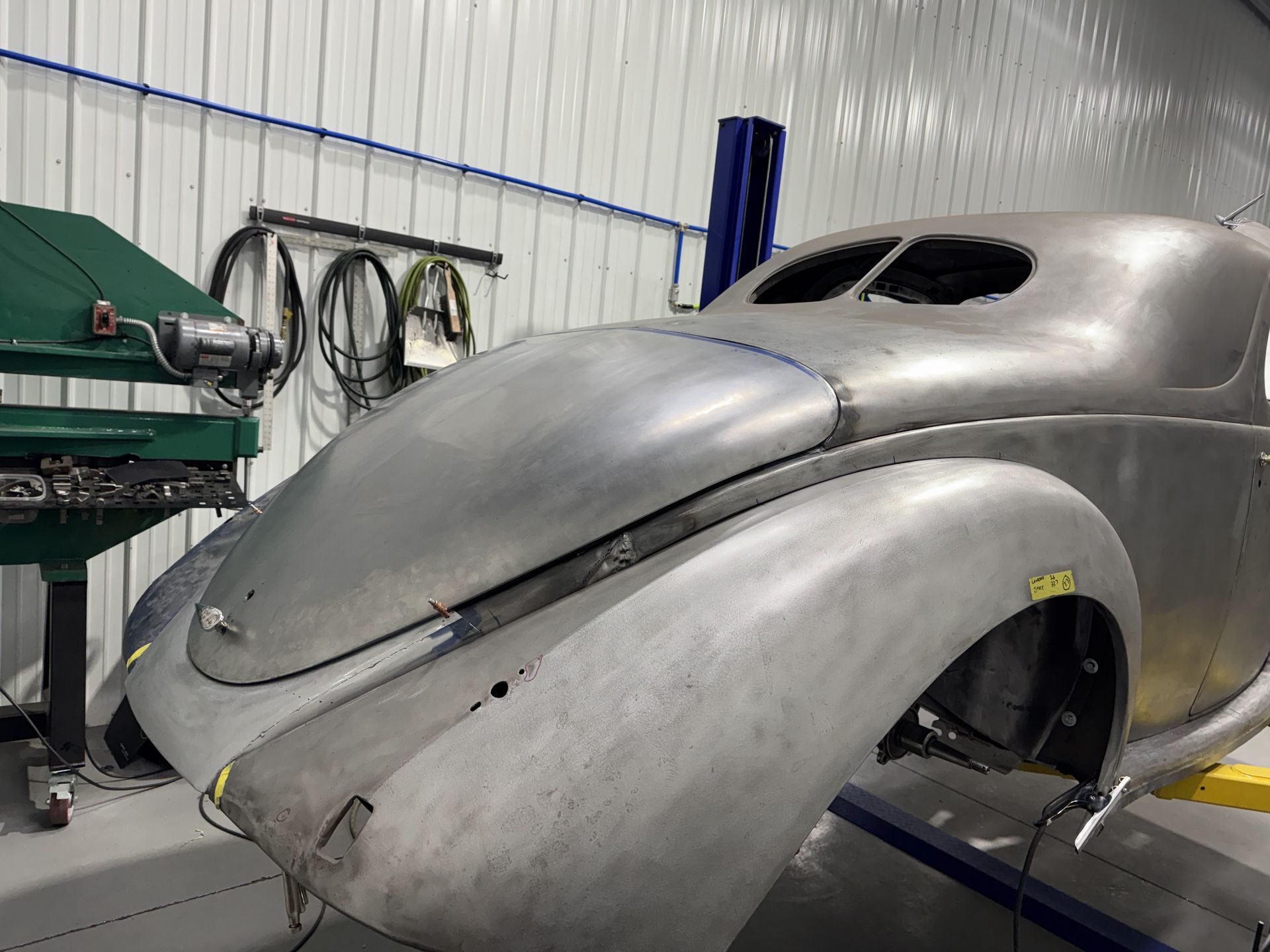 Classic silver car body shell in a workshop, unfinished and propped on supports.