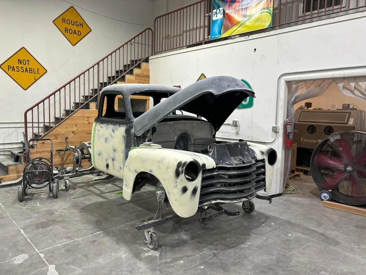 Partially restored vintage pickup truck in a workshop with hood open