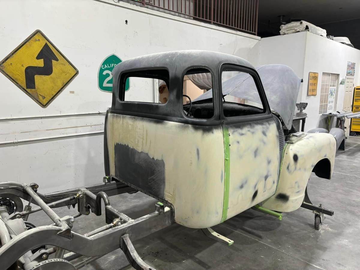 Partially restored old pickup truck cab with gray primer and black roof in a workshop