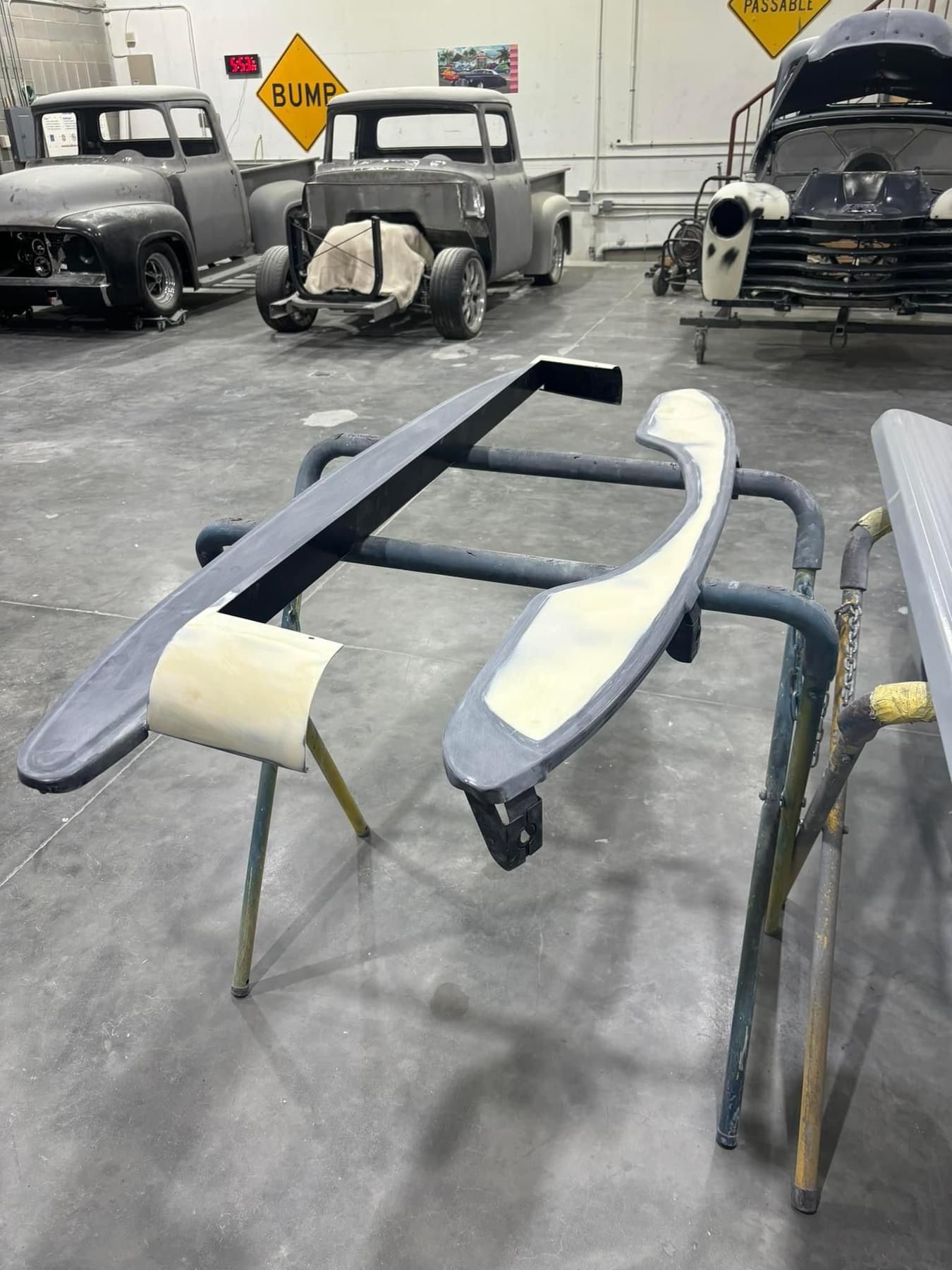 Partially restored vintage car body on stands in an auto shop, with other classic cars in the background