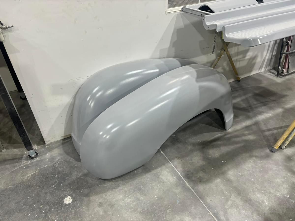 Gray car fender shell propped on a workshop floor beside a wall and table