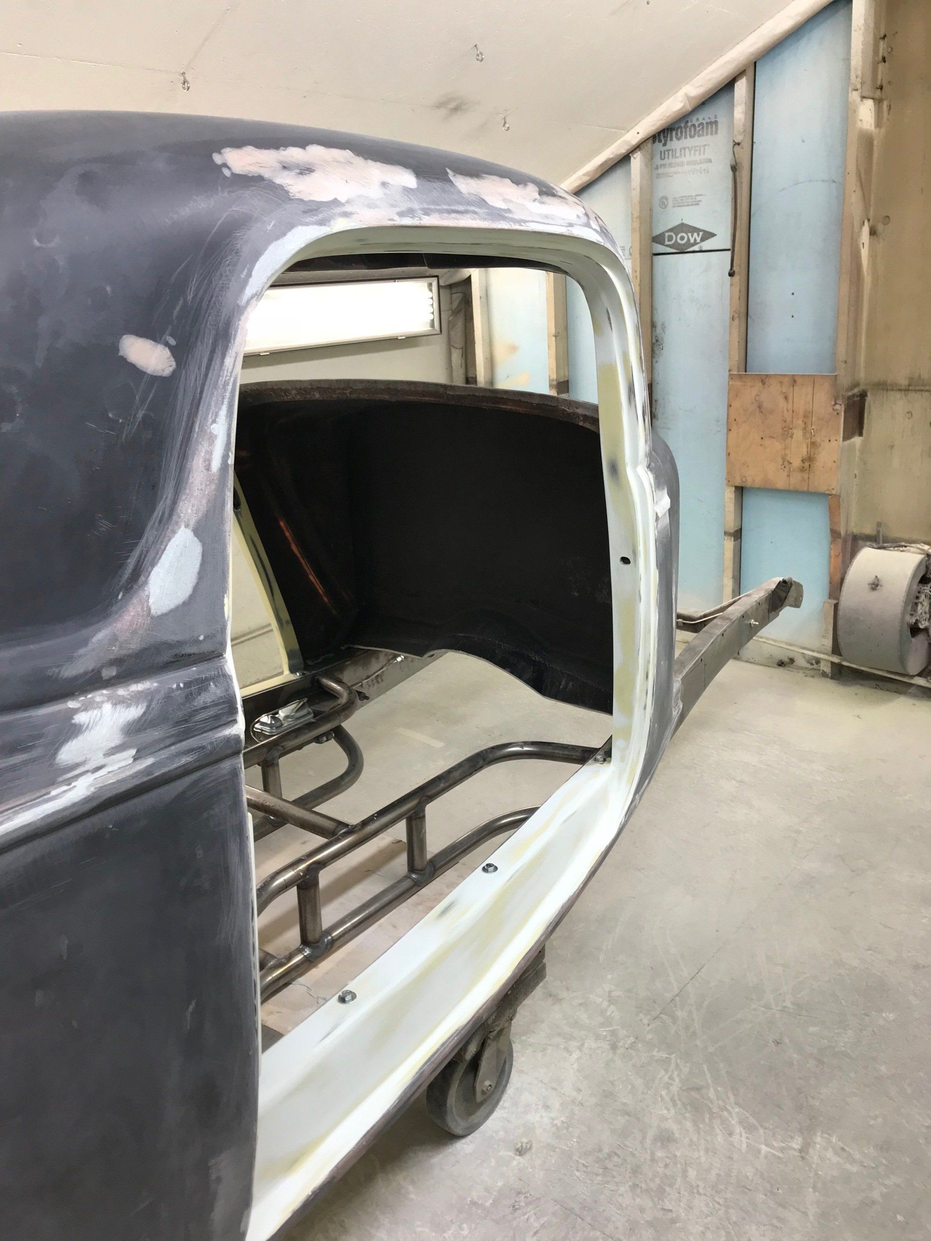 Partially restored car body in a workshop, black top with white lower body and exposed interior frame
