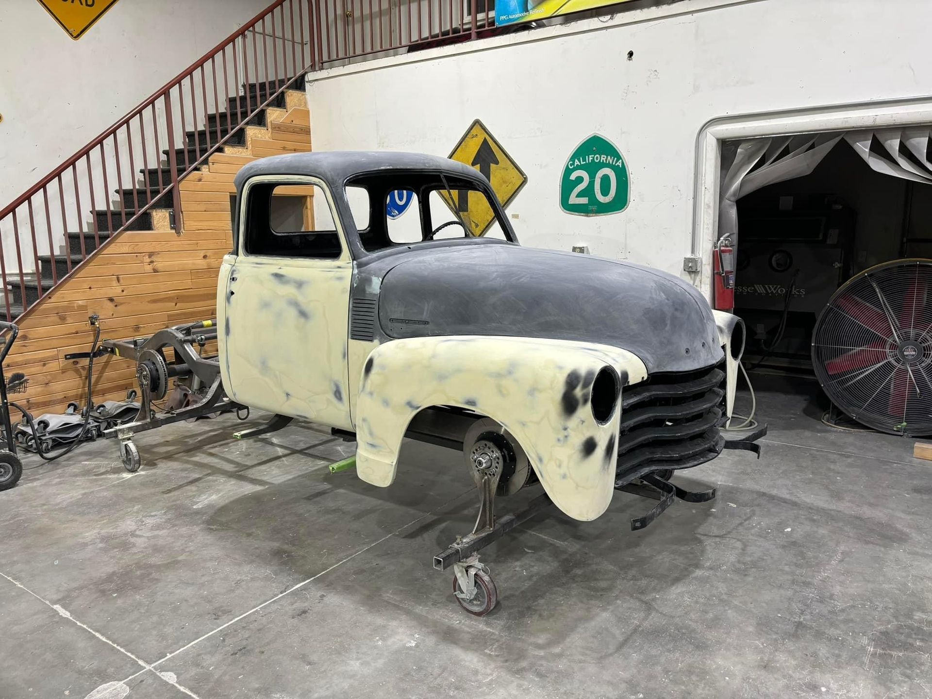Old pickup truck being restored in a garage, with primer on the front and yellow paint on the cab