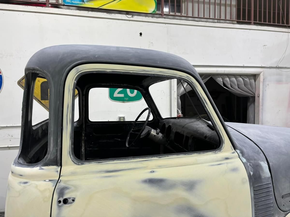 Old cream-and-black vintage pickup truck parked outdoors, viewed through the driver-side window.