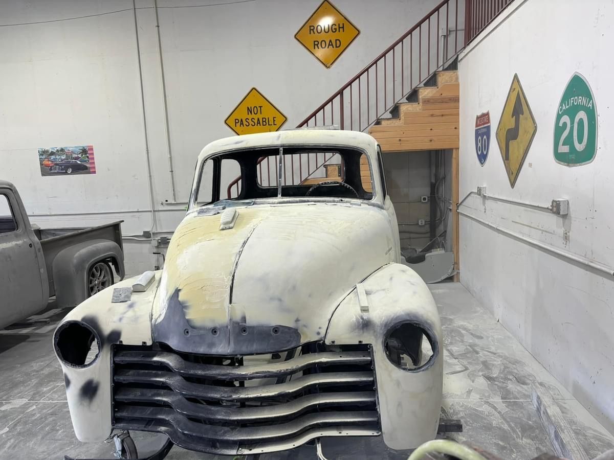 Vintage white pickup truck in a dusty garage, front view with stacked grille and empty headlights