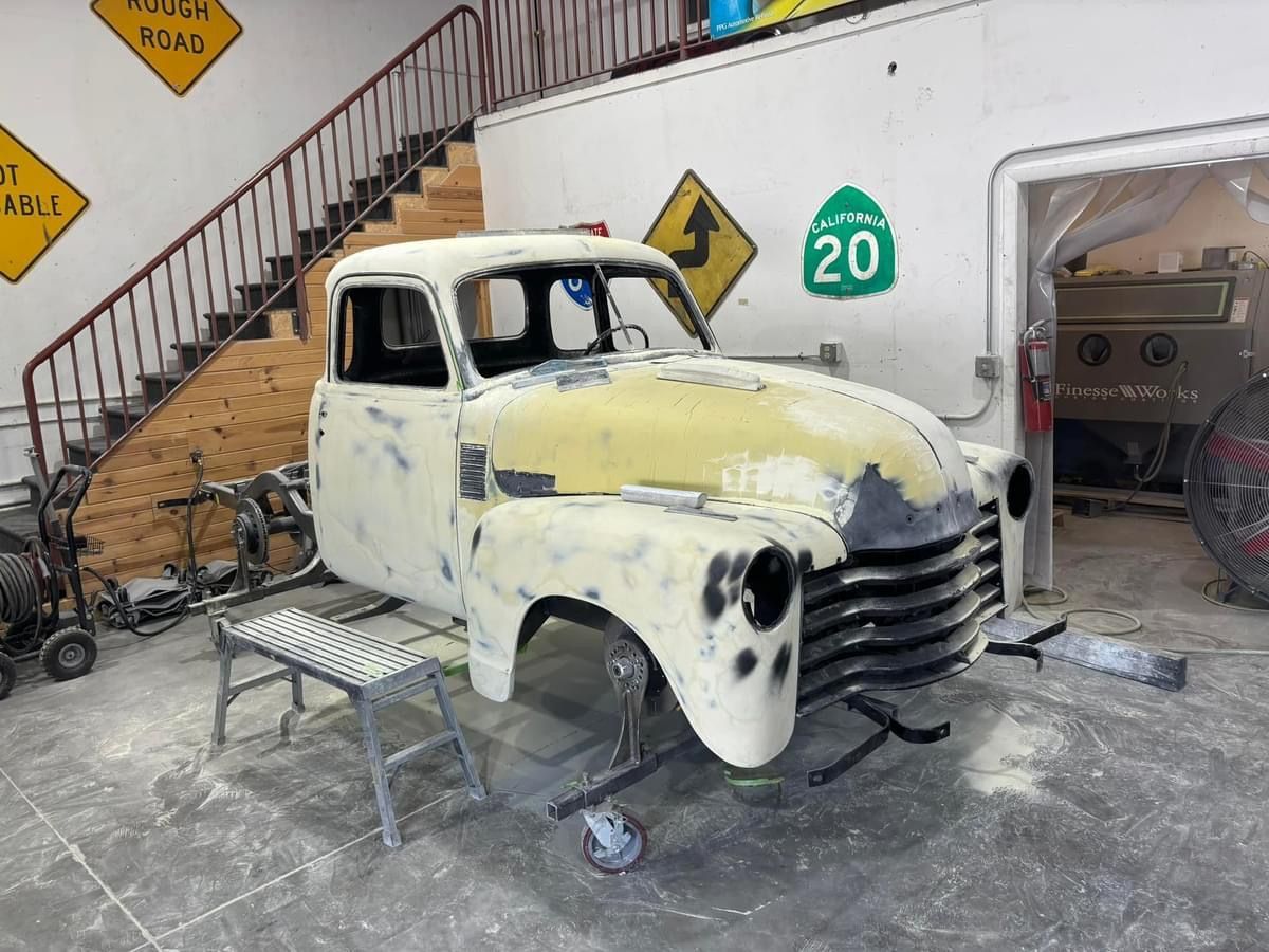 Old white pickup truck under repair in a garage, with primer patches and parts removed