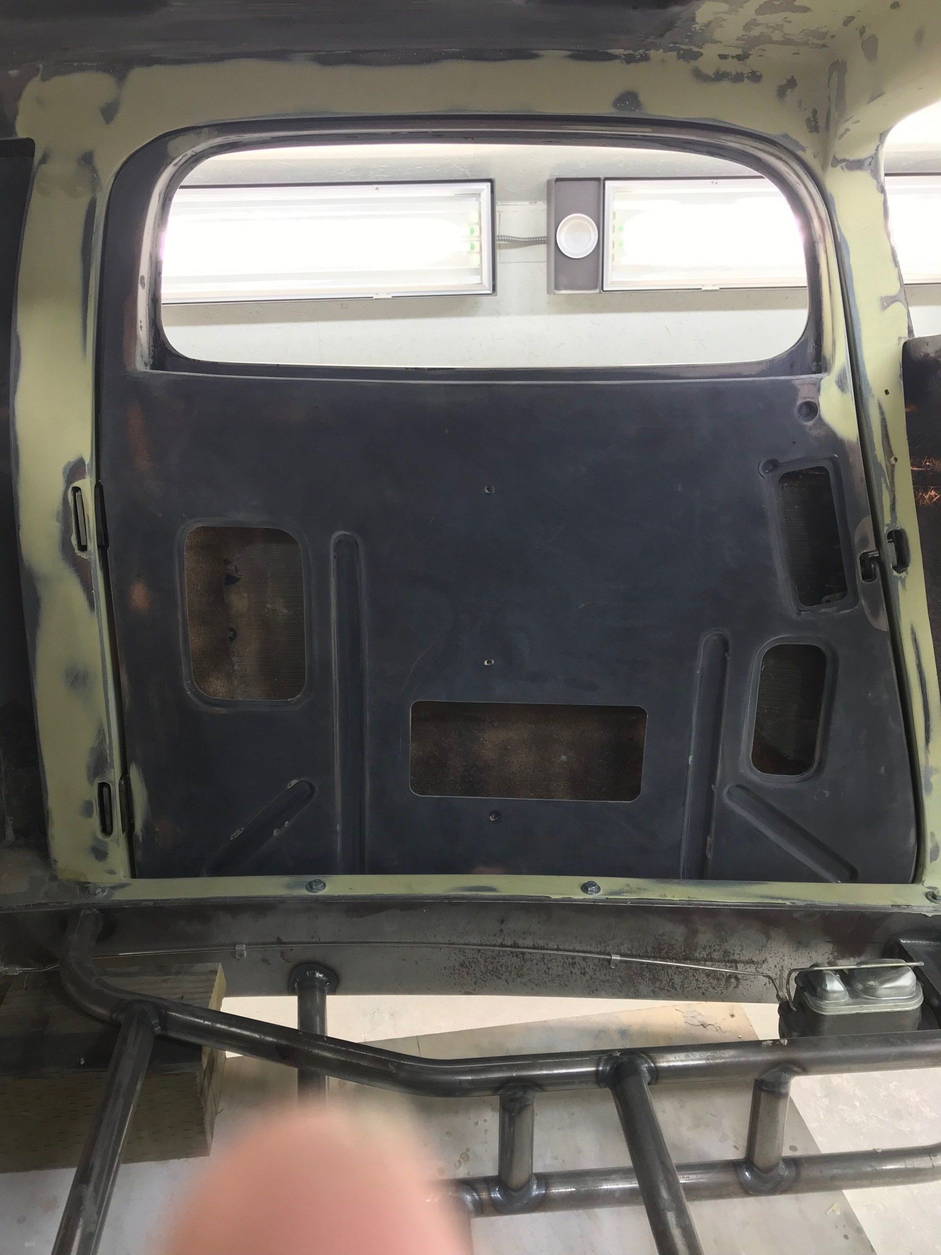 Inside a vehicle, a dark padded rear panel with cutouts and window openings is shown.