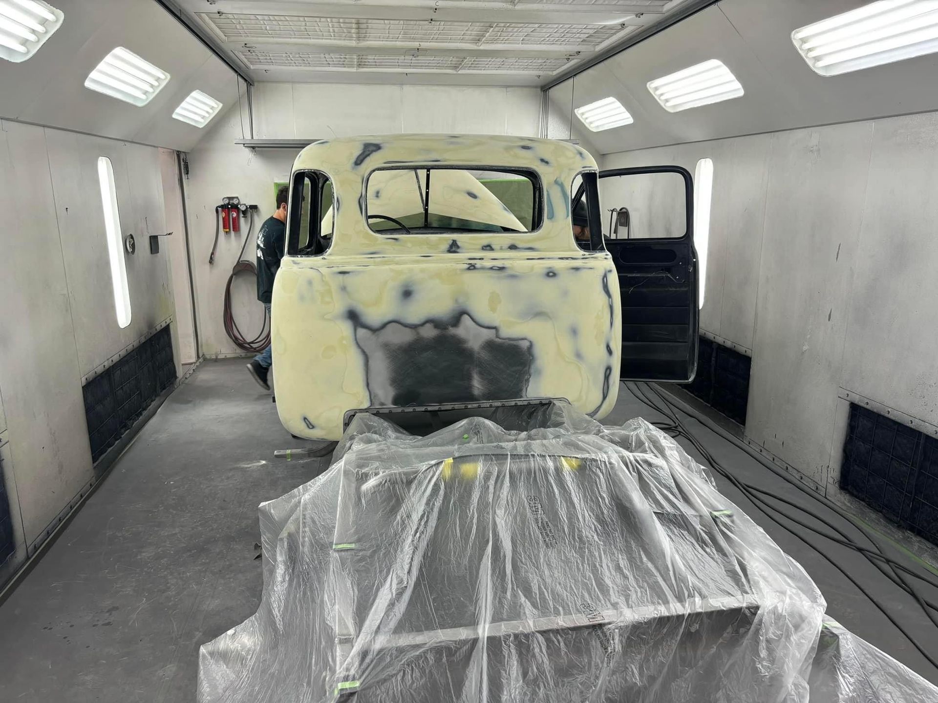 Vintage van body in a white paint booth, partially sanded and masked for restoration.