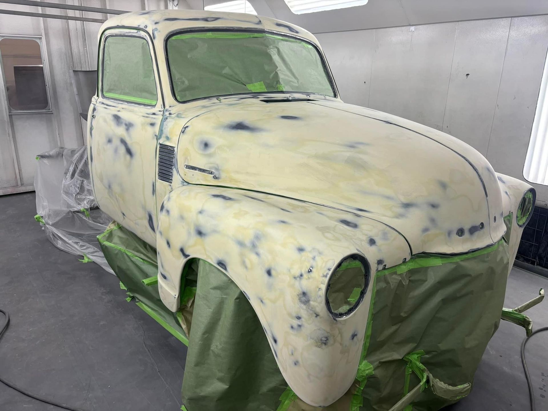 Primer-coated vintage car body in a spray booth, masked for painting.