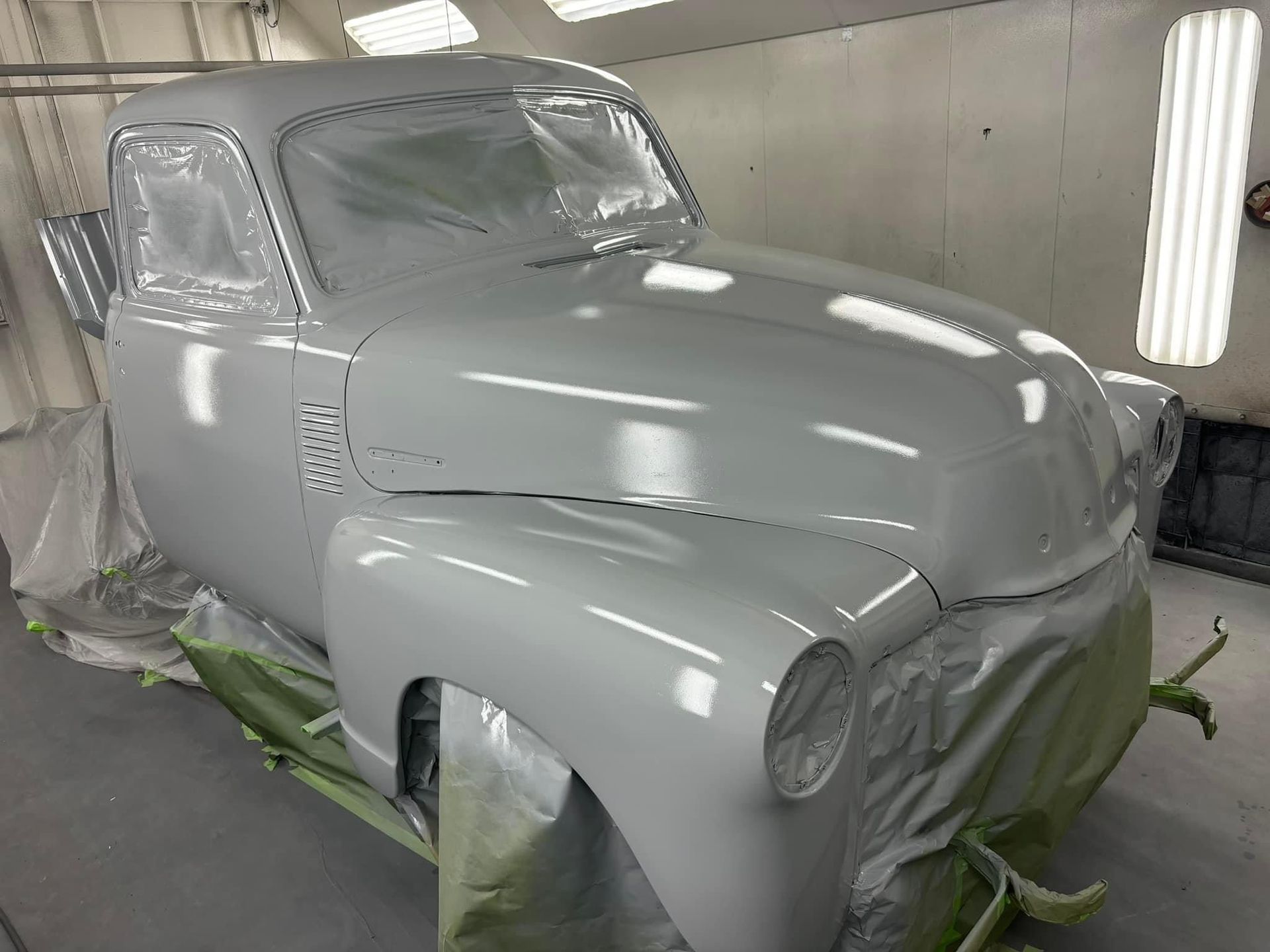 Gray car body in a spray booth, covered for painting and masked with protective sheets.