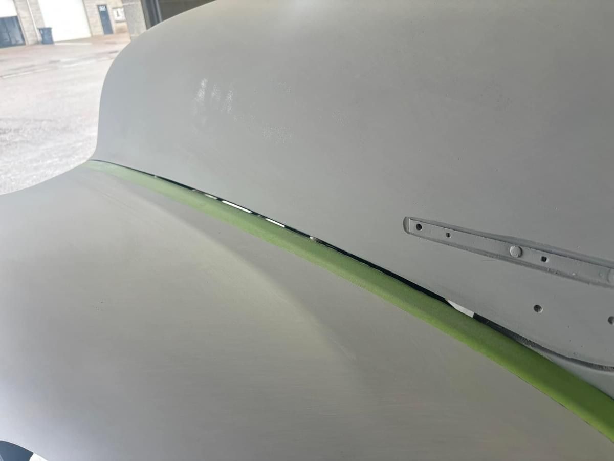 Close-up of a gray car body panel with a green seam or masking line along the edge.