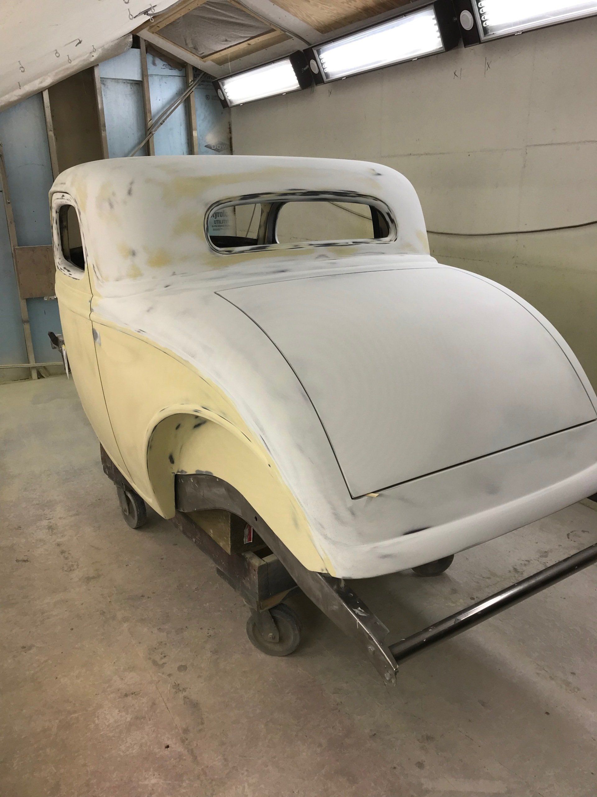 White vintage car body shell in a workshop, missing wheels and parts, under restoration