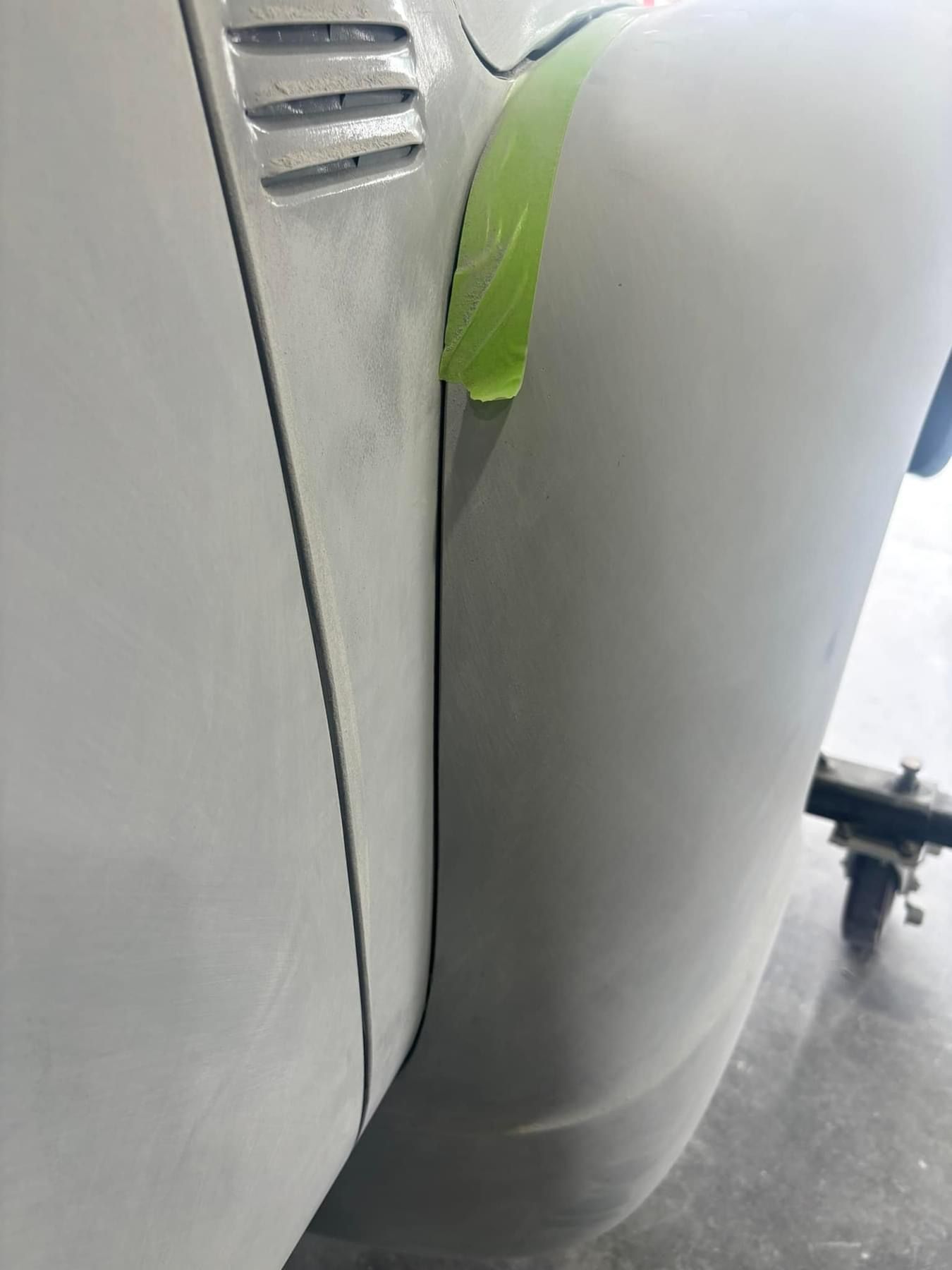 Close-up of a white vehicle bumper with a green tape mark near the edge