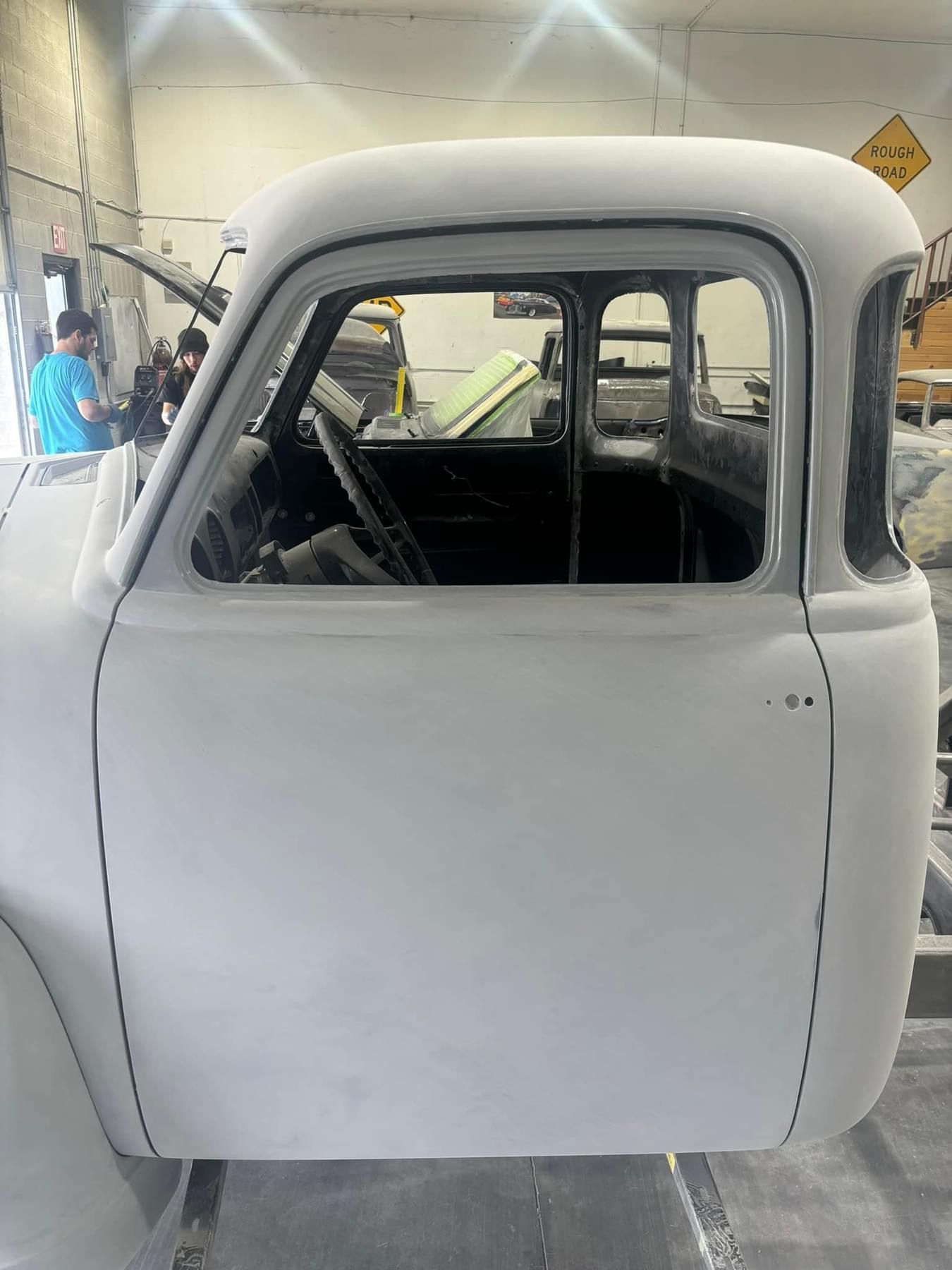 White vintage car body in a workshop garage, shown from the side with an open door frame.