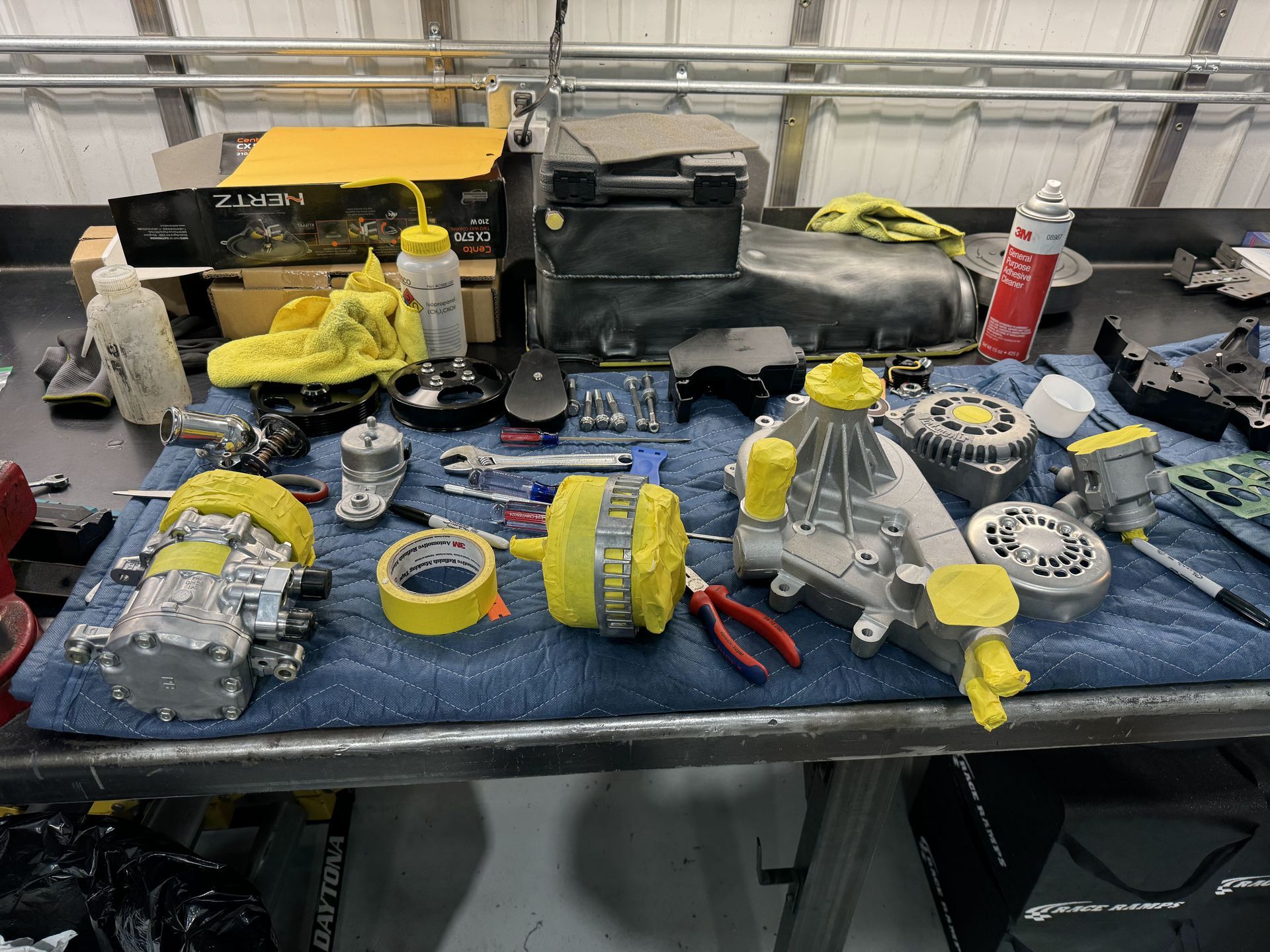 Workbench covered with automotive parts wrapped in yellow tape inside a garage-like shop.