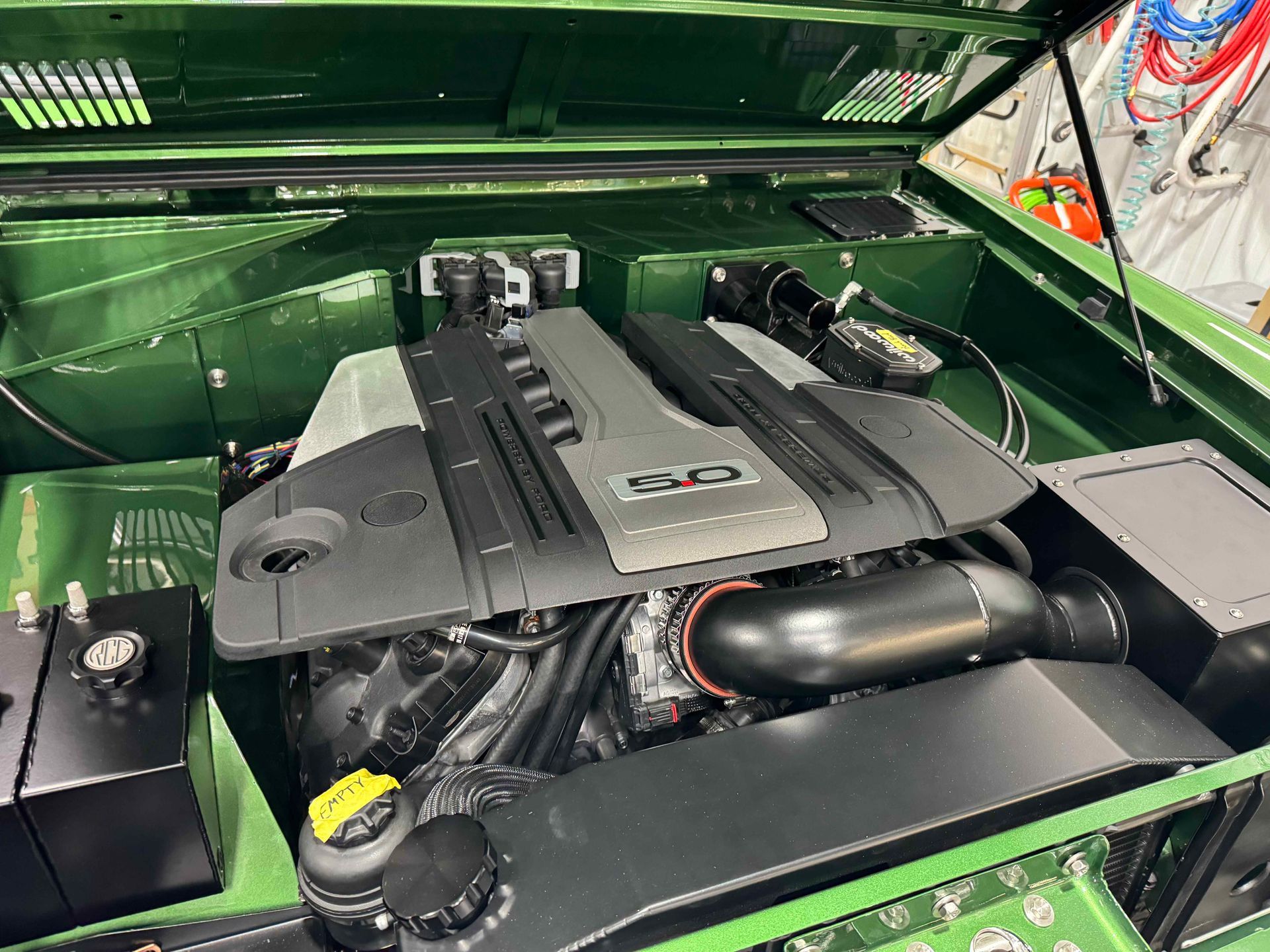 Open green car hood showing a clean engine bay with black and silver engine cover.
